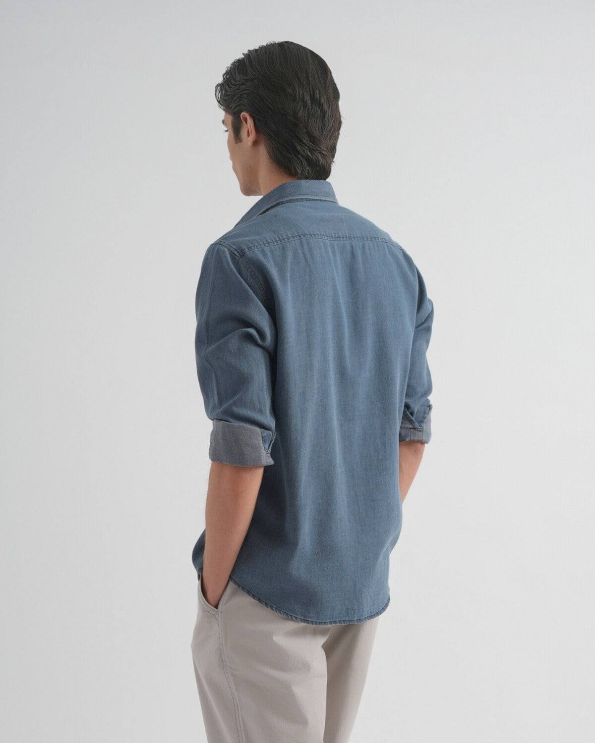 Person wearing a blue denim shirt and beige pants on a white background