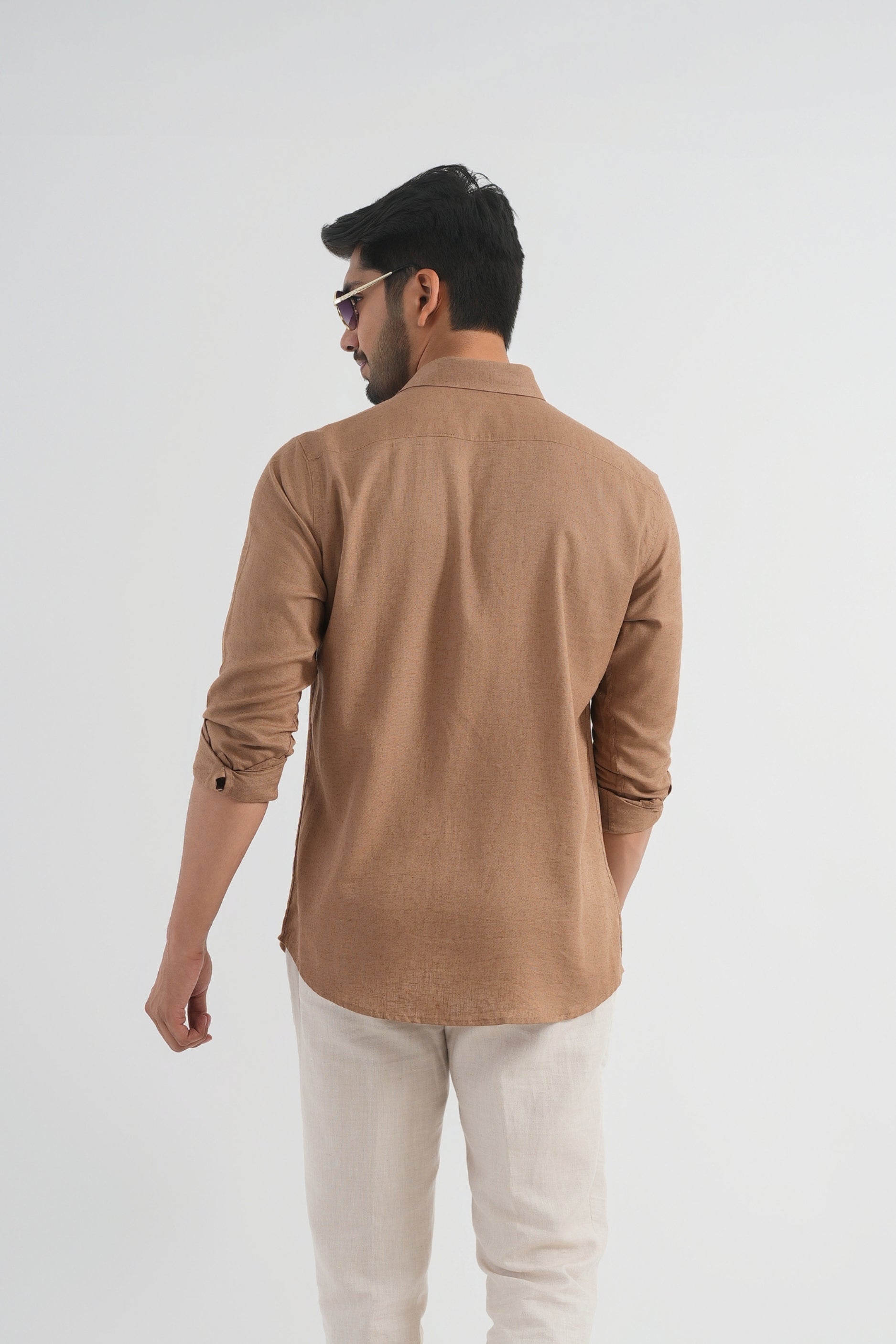 Man wearing a brown shirt and light-colored pants on a white background