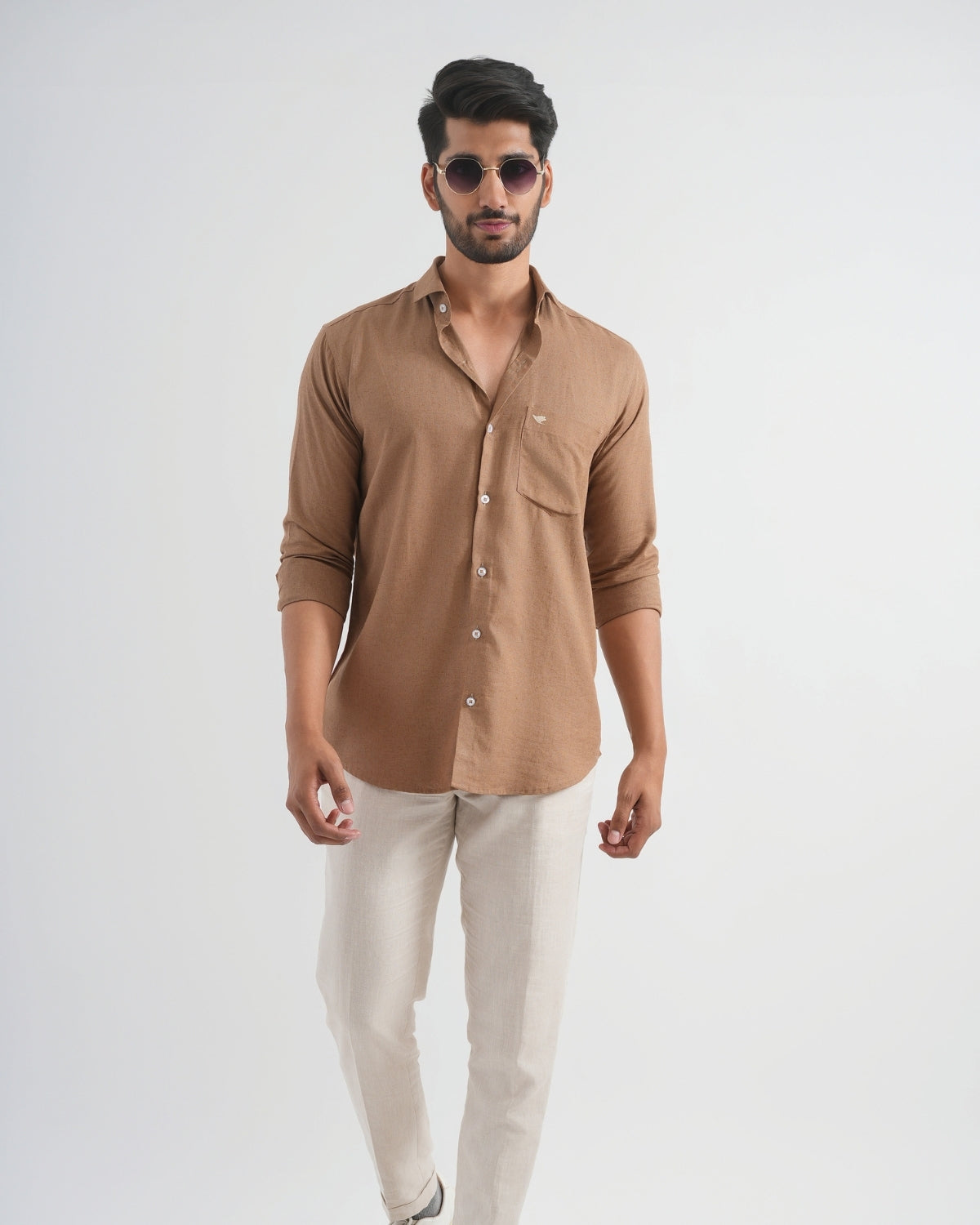 Man wearing a brown shirt and beige pants on a white background