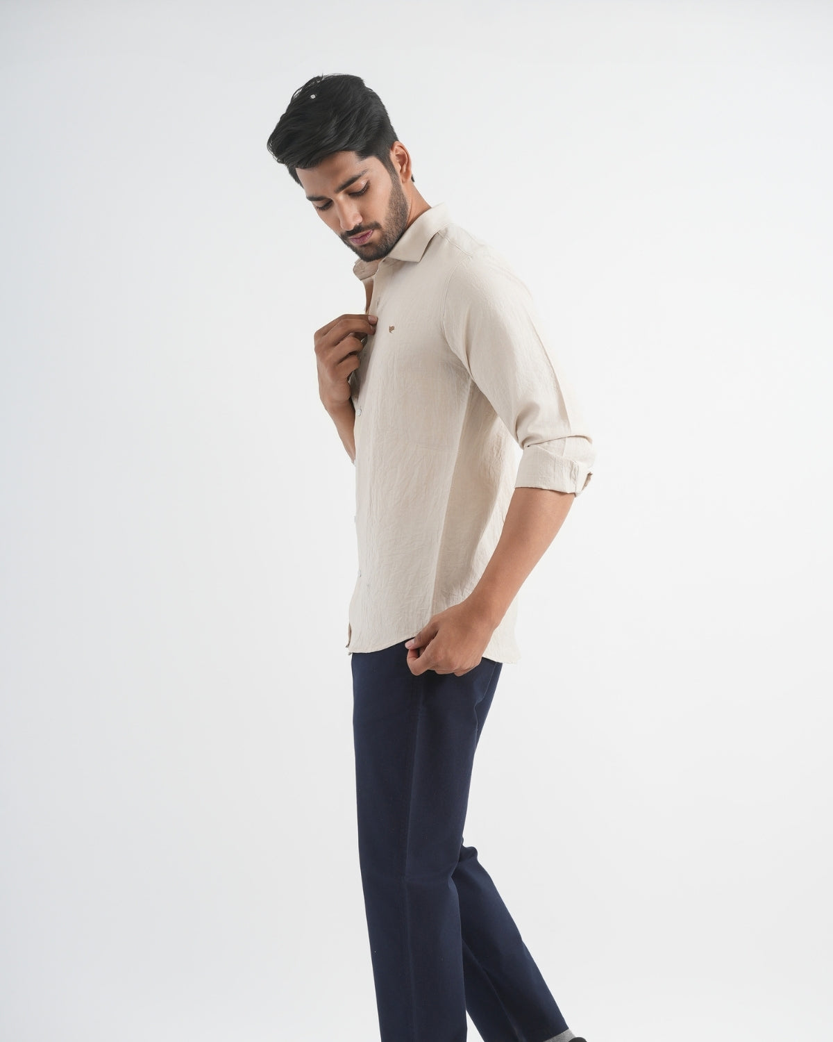 Man wearing a beige shirt and dark pants on a white background