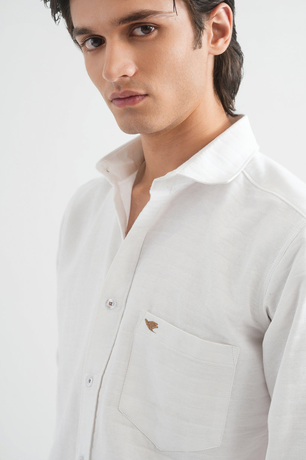 Man wearing a light gray shirt with a small logo on a white background