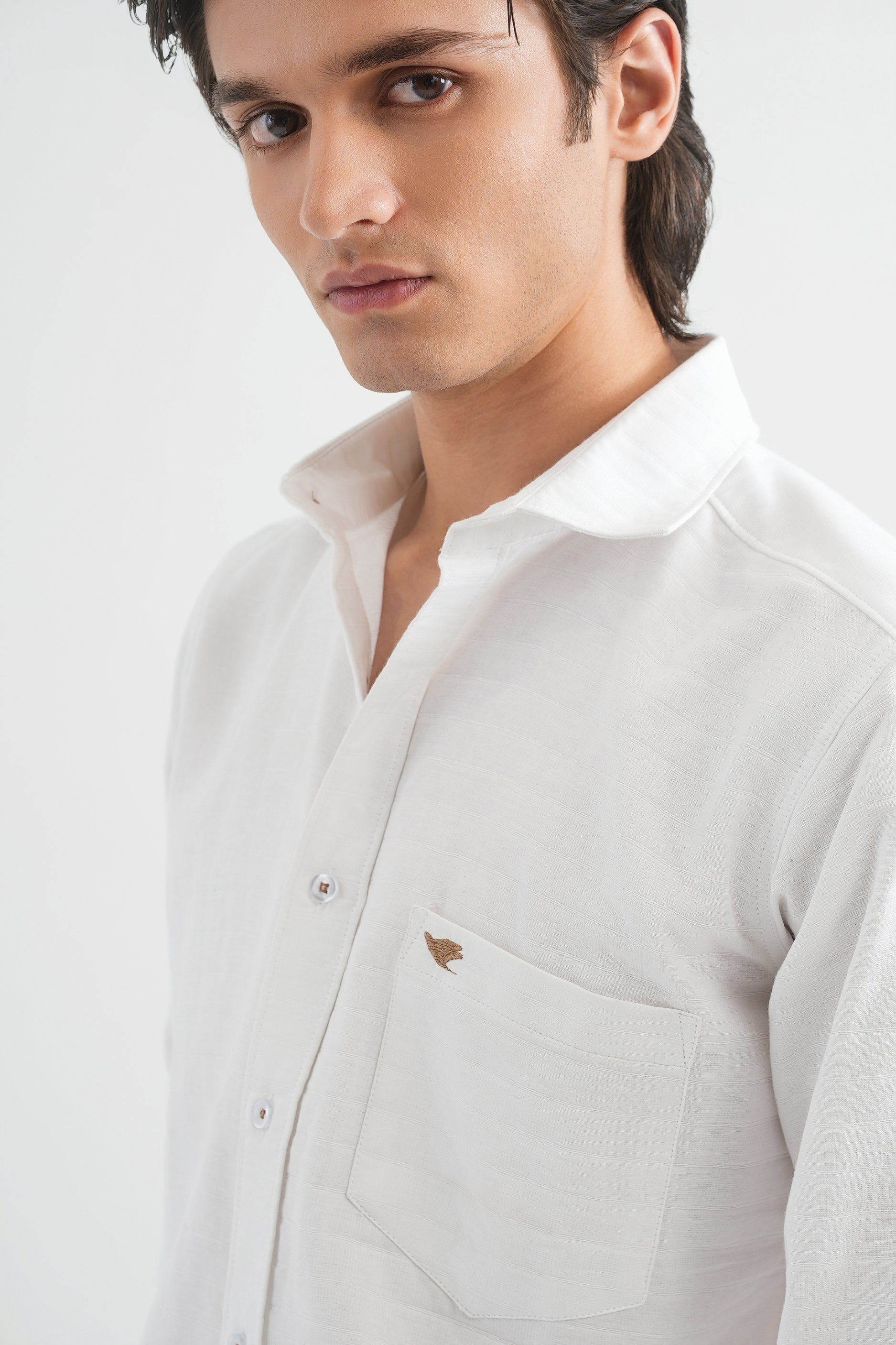 Man wearing a light gray shirt with a small logo on a white background