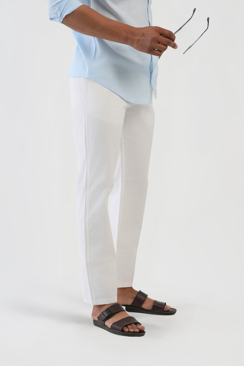 Person wearing a light blue shirt, white pants, and black sandals on a white background
