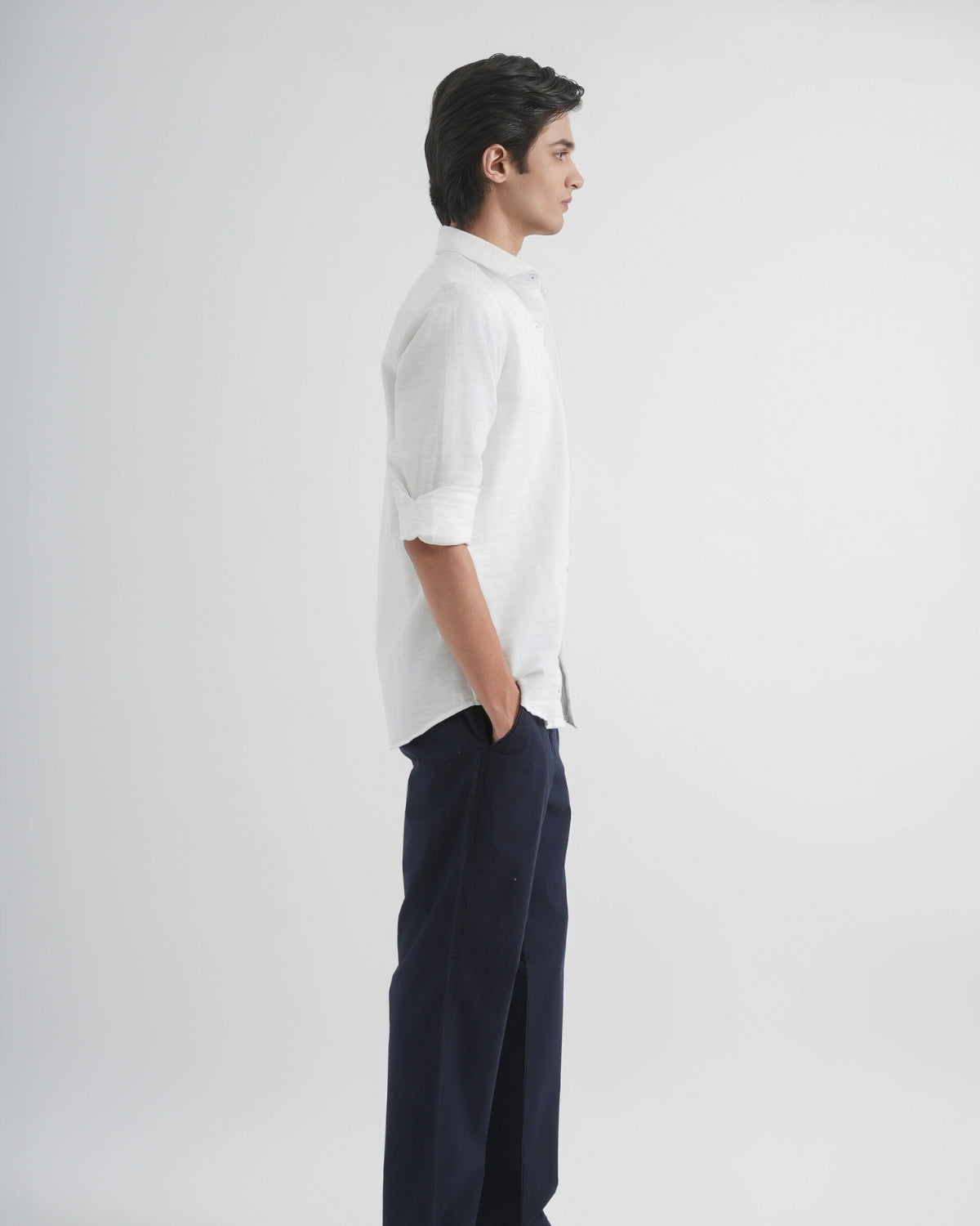 Person wearing a white shirt and dark pants on a plain background