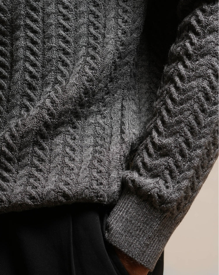 Close-up of a gray cable knit sweater with a blurred background