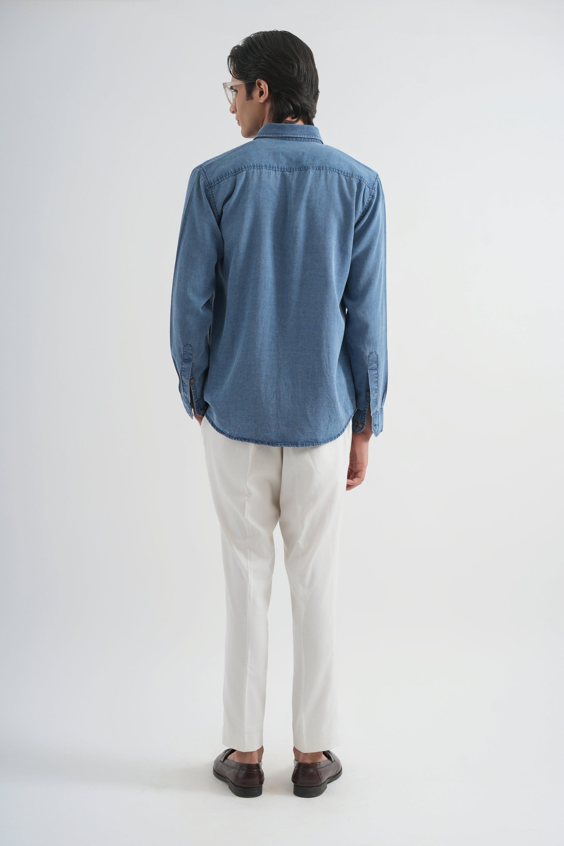 Man wearing a blue shirt and white pants on a white background