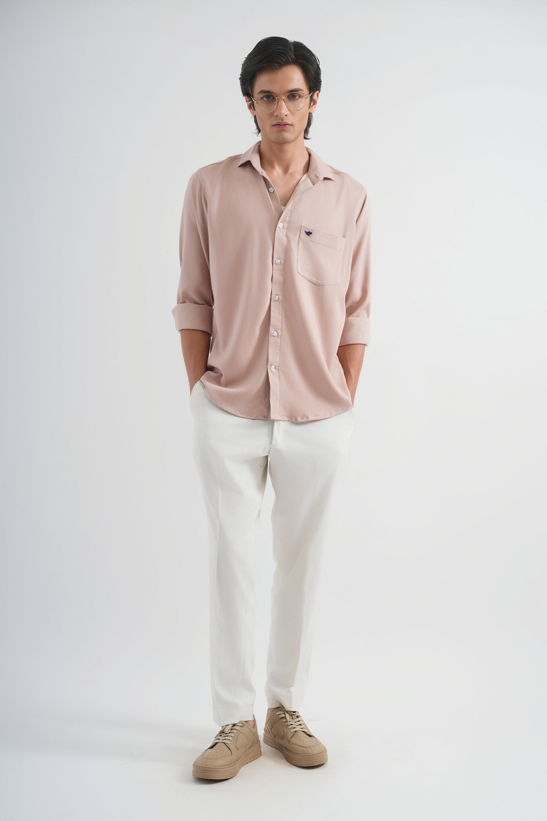 Man wearing a light pink shirt, white pants, and brown shoes on a white background