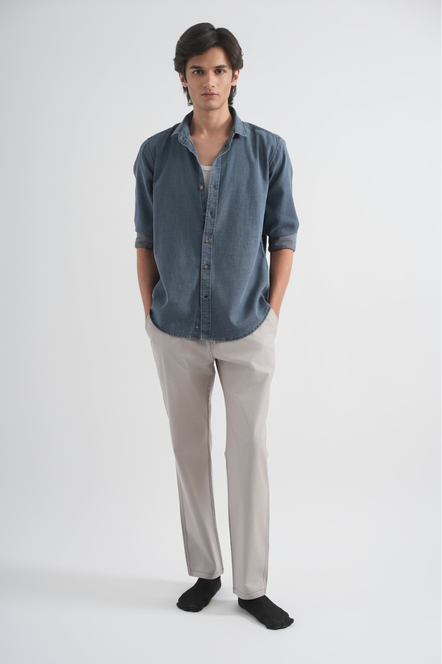 Man wearing a blue shirt and beige pants on a white background