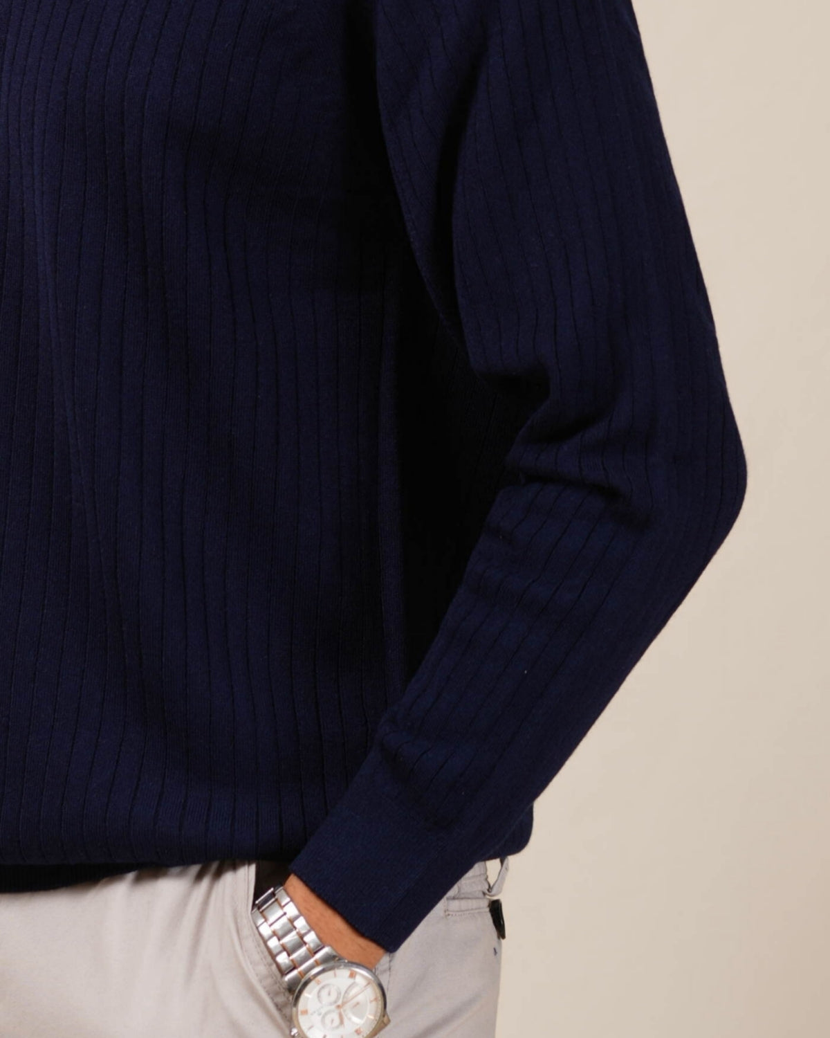 Man wearing a navy blue long-sleeve shirt and light gray pants against a beige background