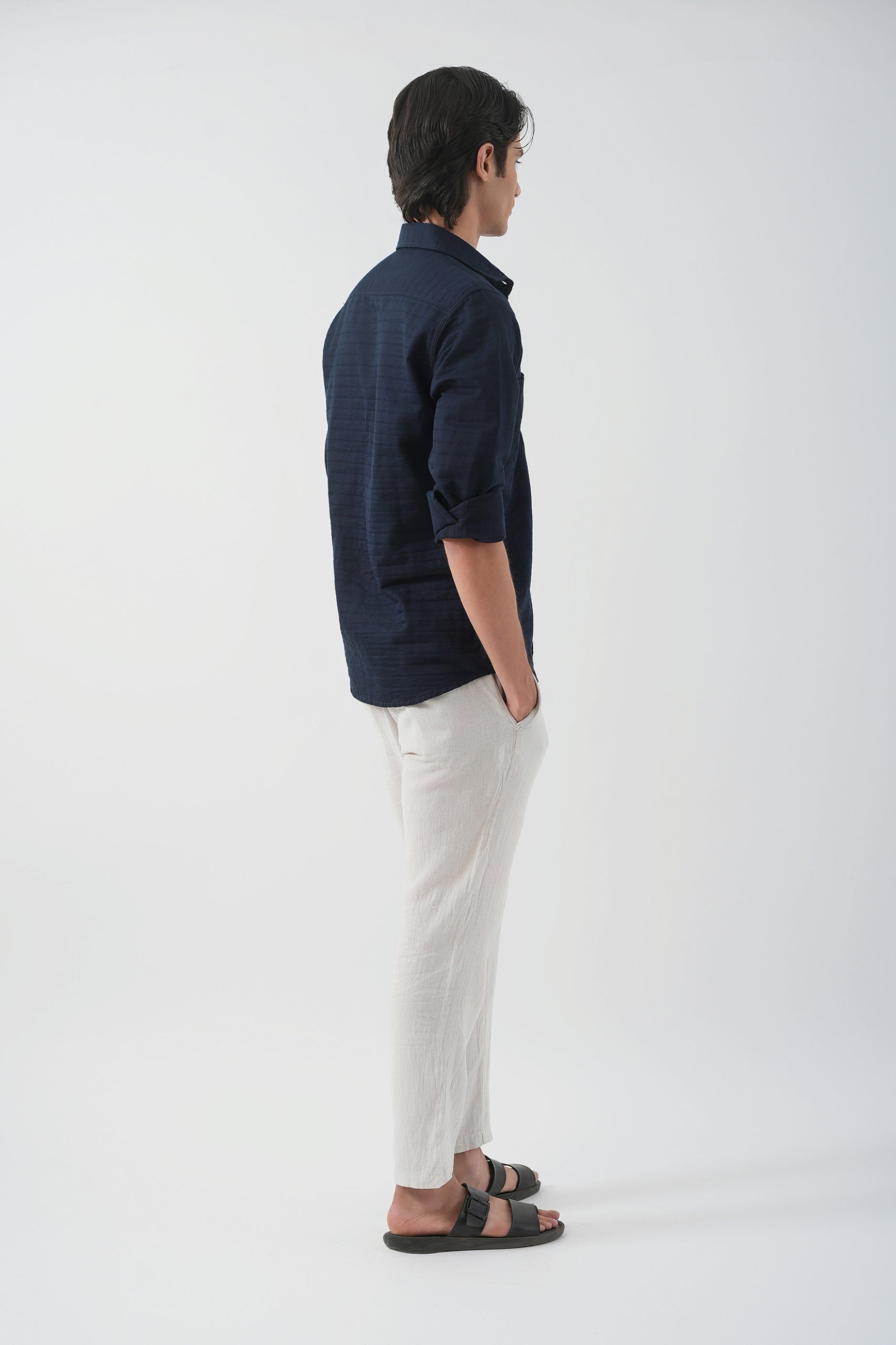 Person wearing a navy shirt and white pants standing against a white background
