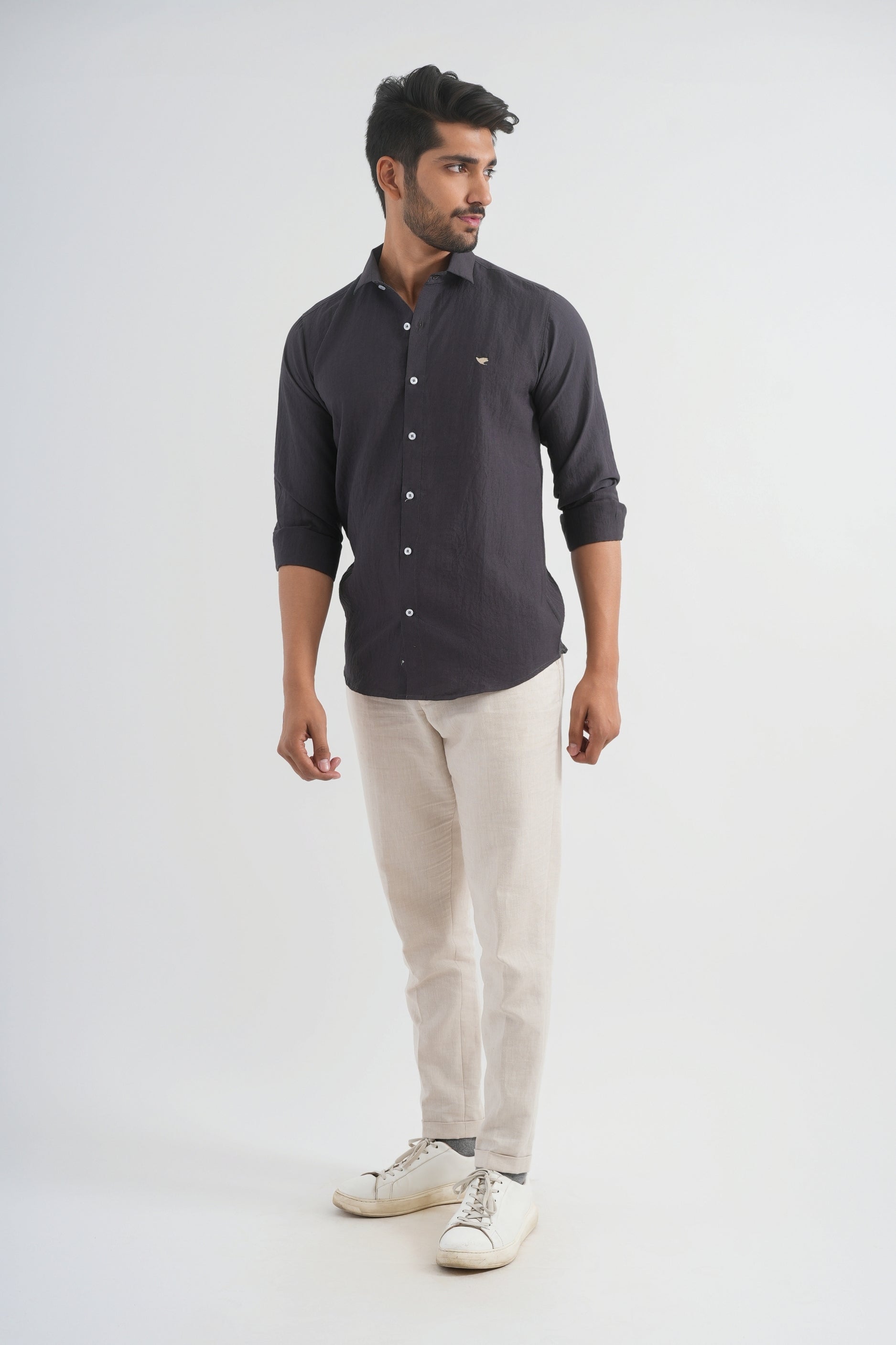 Man wearing a dark gray button-up shirt and beige pants on a white background