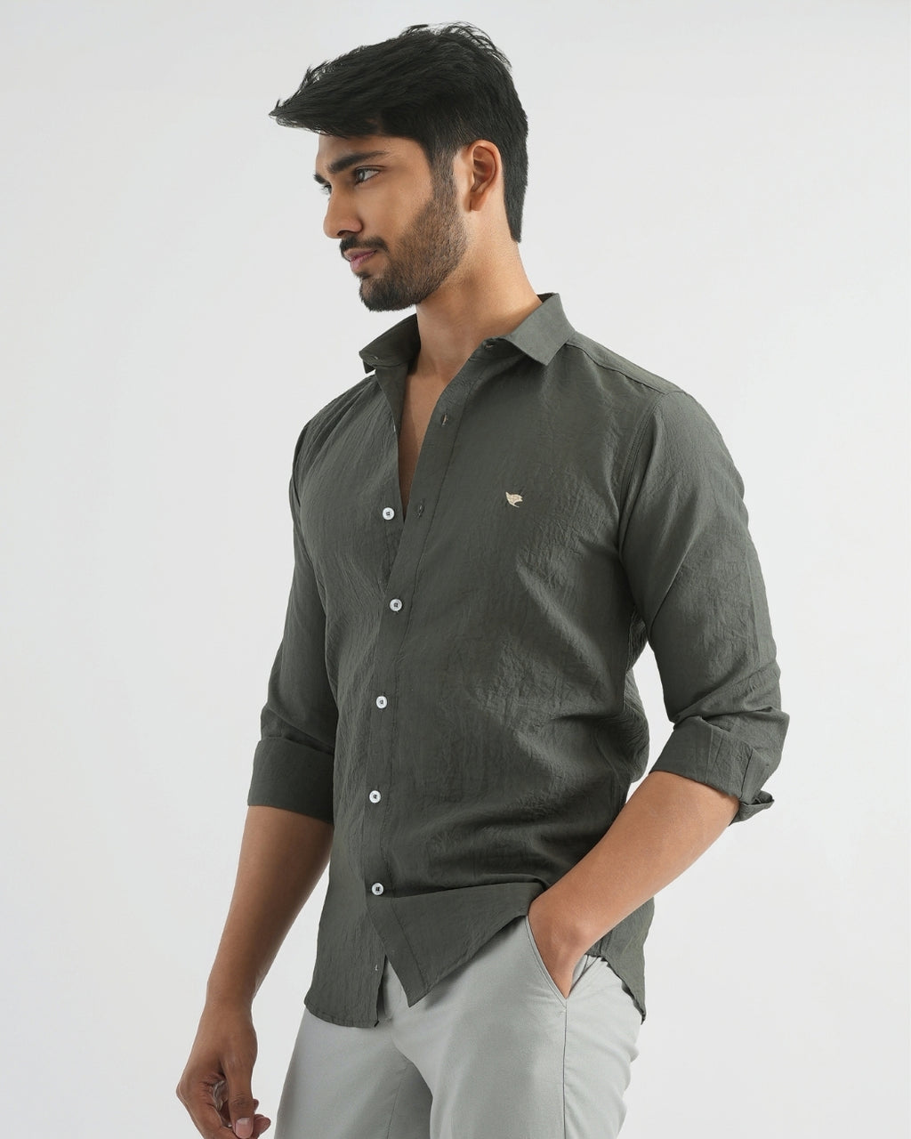 Man wearing a dark green shirt with rolled-up sleeves on a light gray background