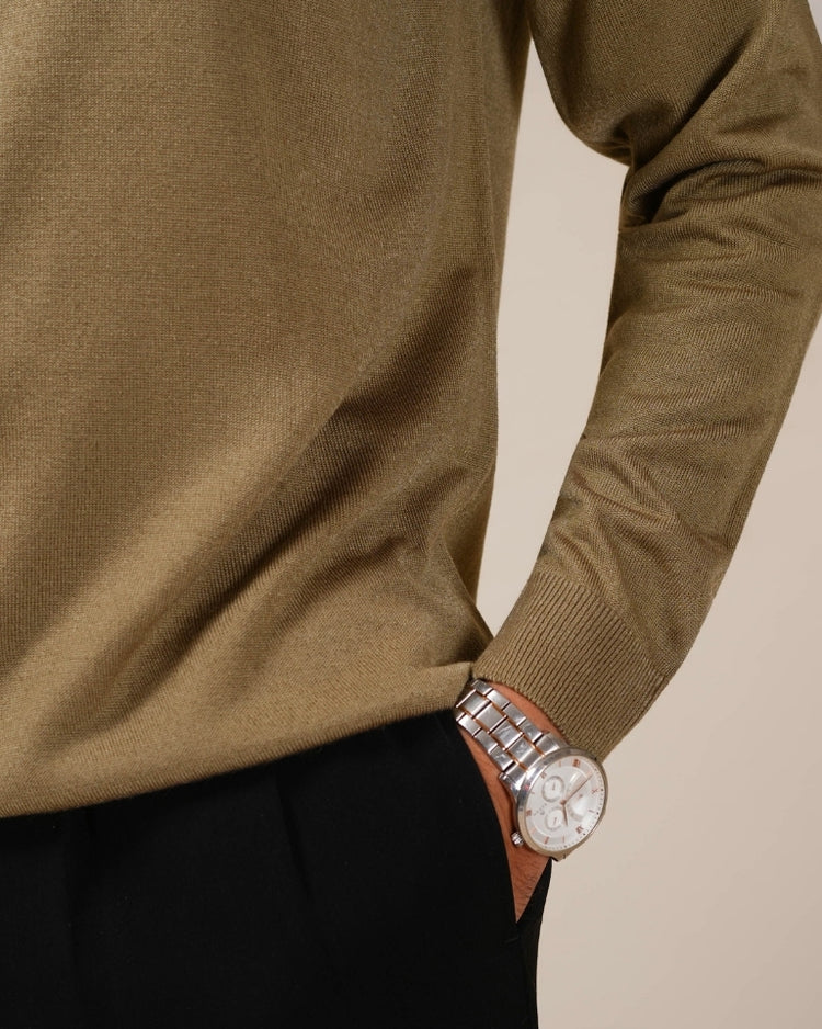Close-up of a person wearing a brown sweater with a watch on a beige background