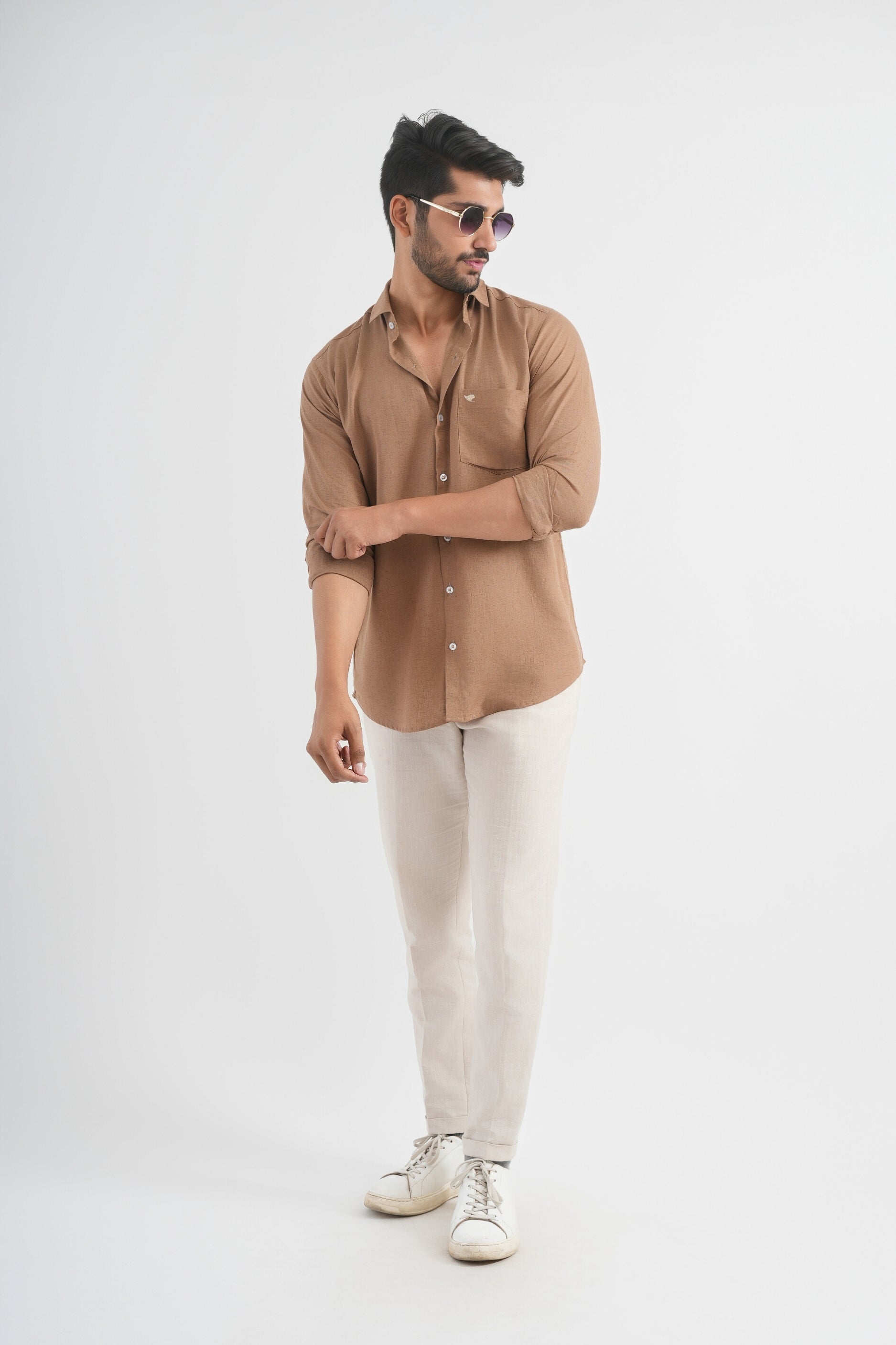 Man wearing a brown shirt, beige pants, and white sneakers on a white background
