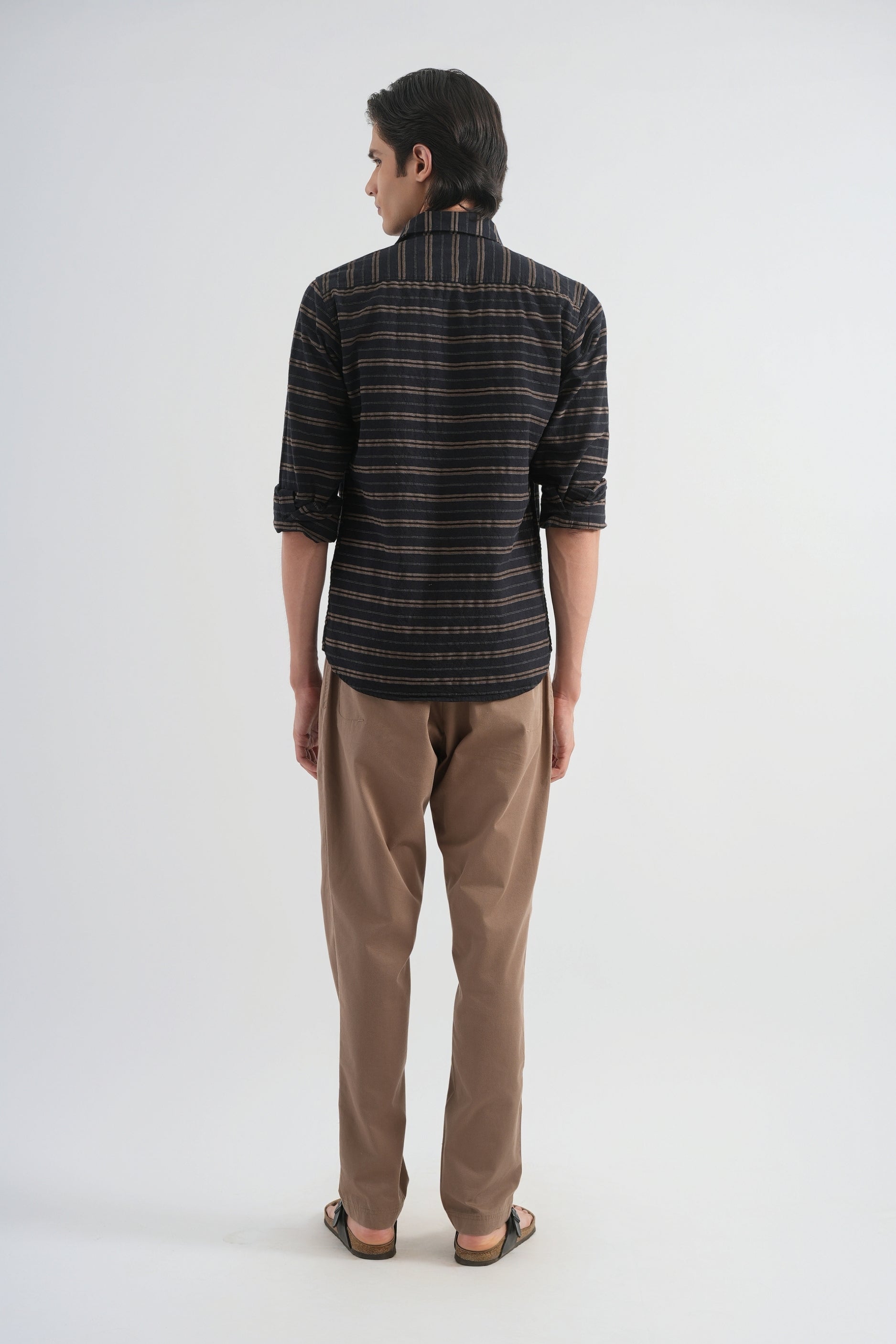 Person wearing a striped shirt and brown pants on a white background