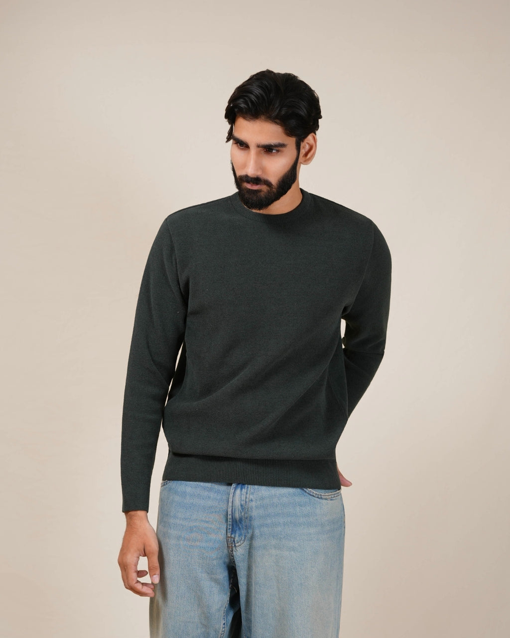 Man wearing a dark green sweater and light blue jeans against a beige background