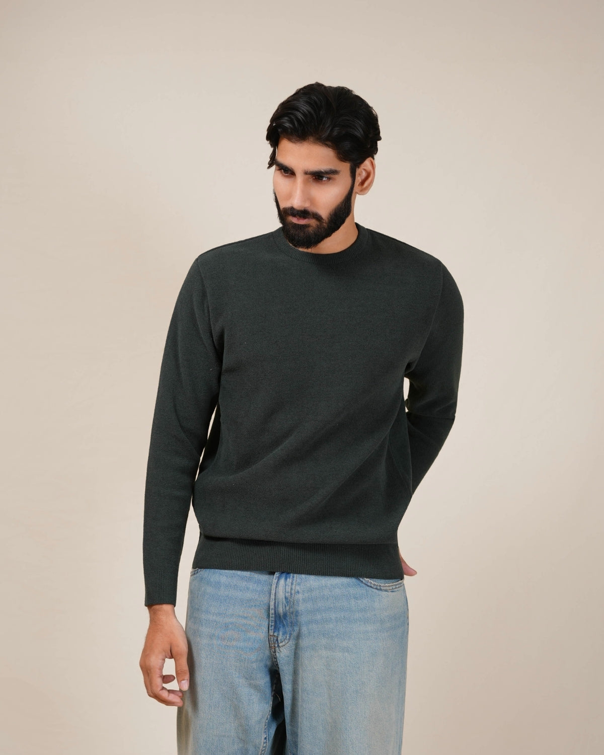 Man wearing a dark green sweater and light blue jeans against a beige background