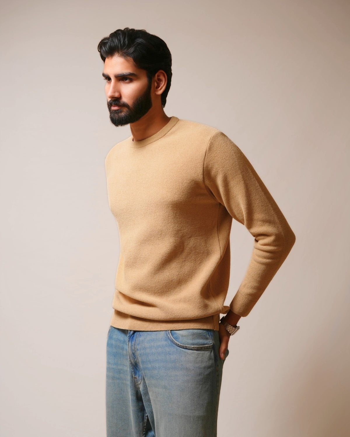 Man wearing a beige sweater and blue jeans against a plain background