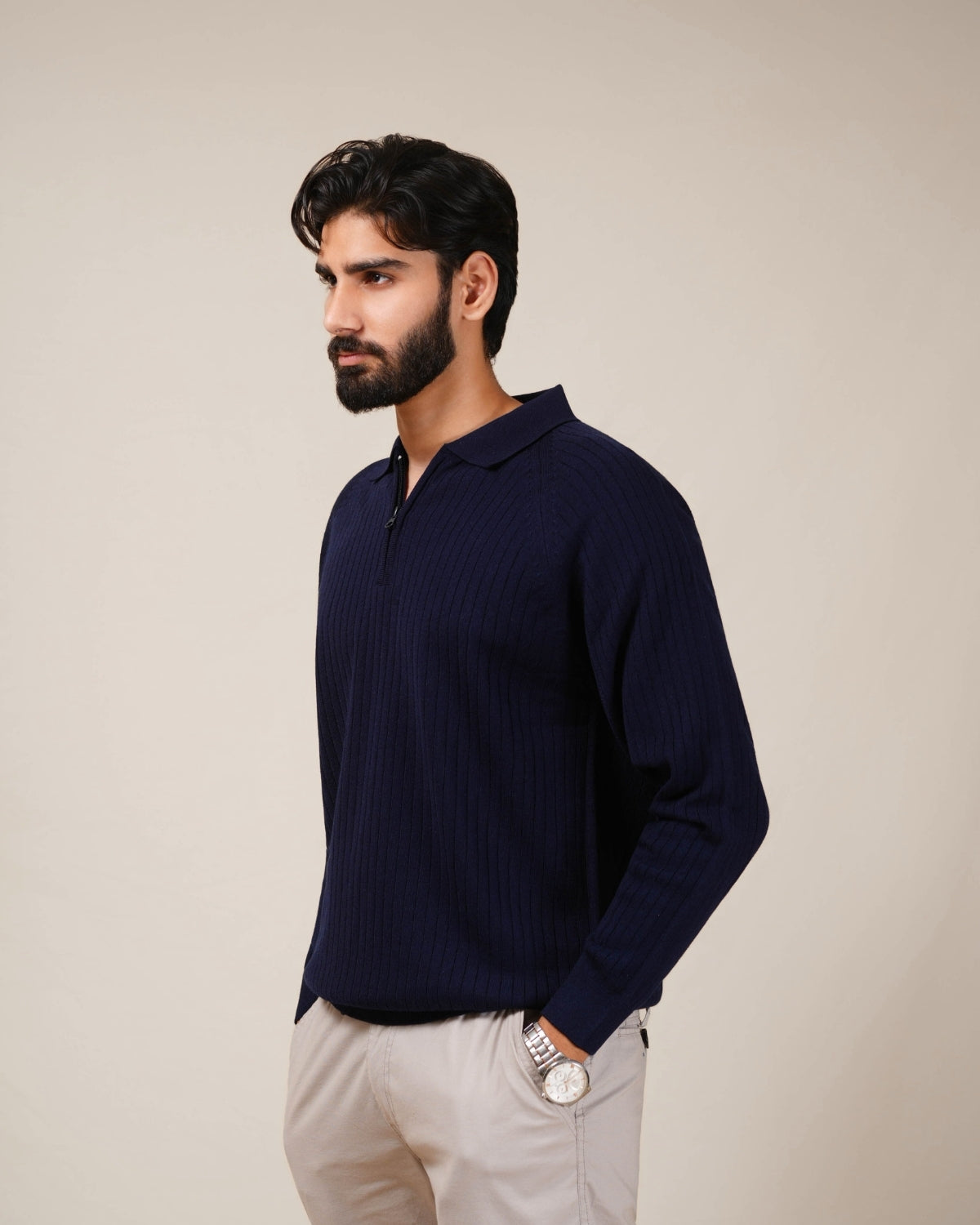 Man wearing a navy long-sleeve shirt and light-colored pants against a beige background