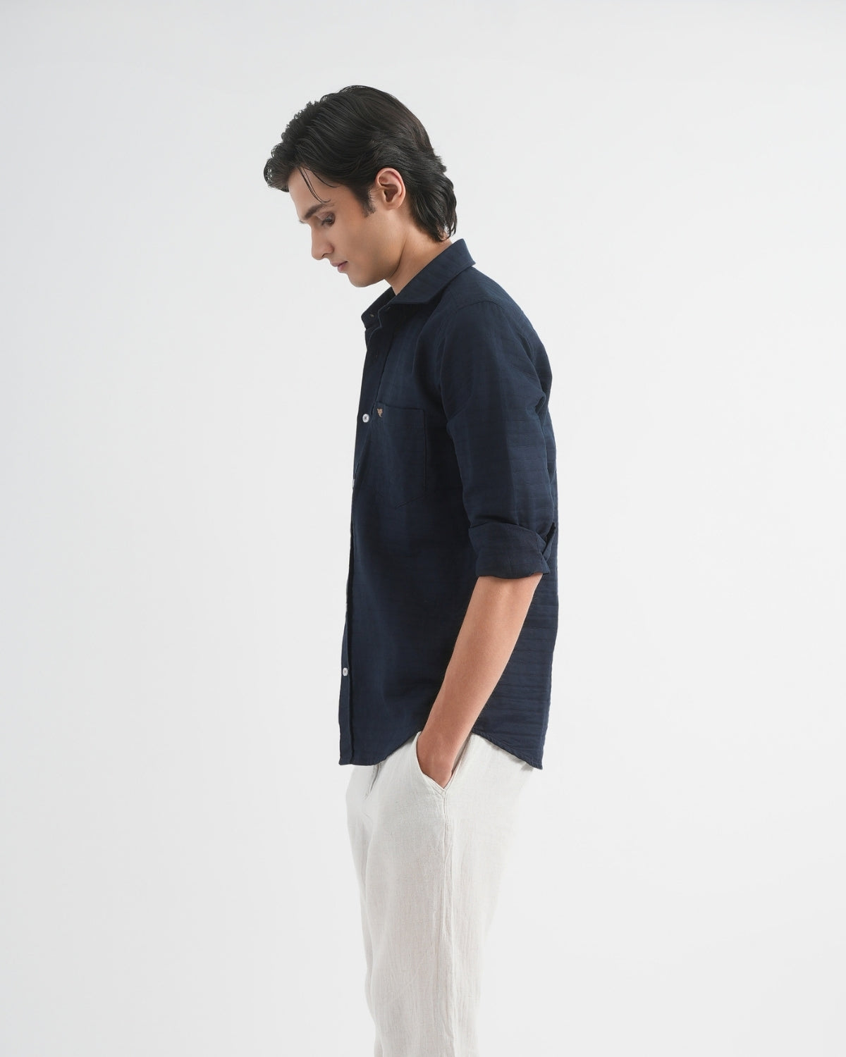Man wearing a dark blue shirt and white pants on a light gray background
