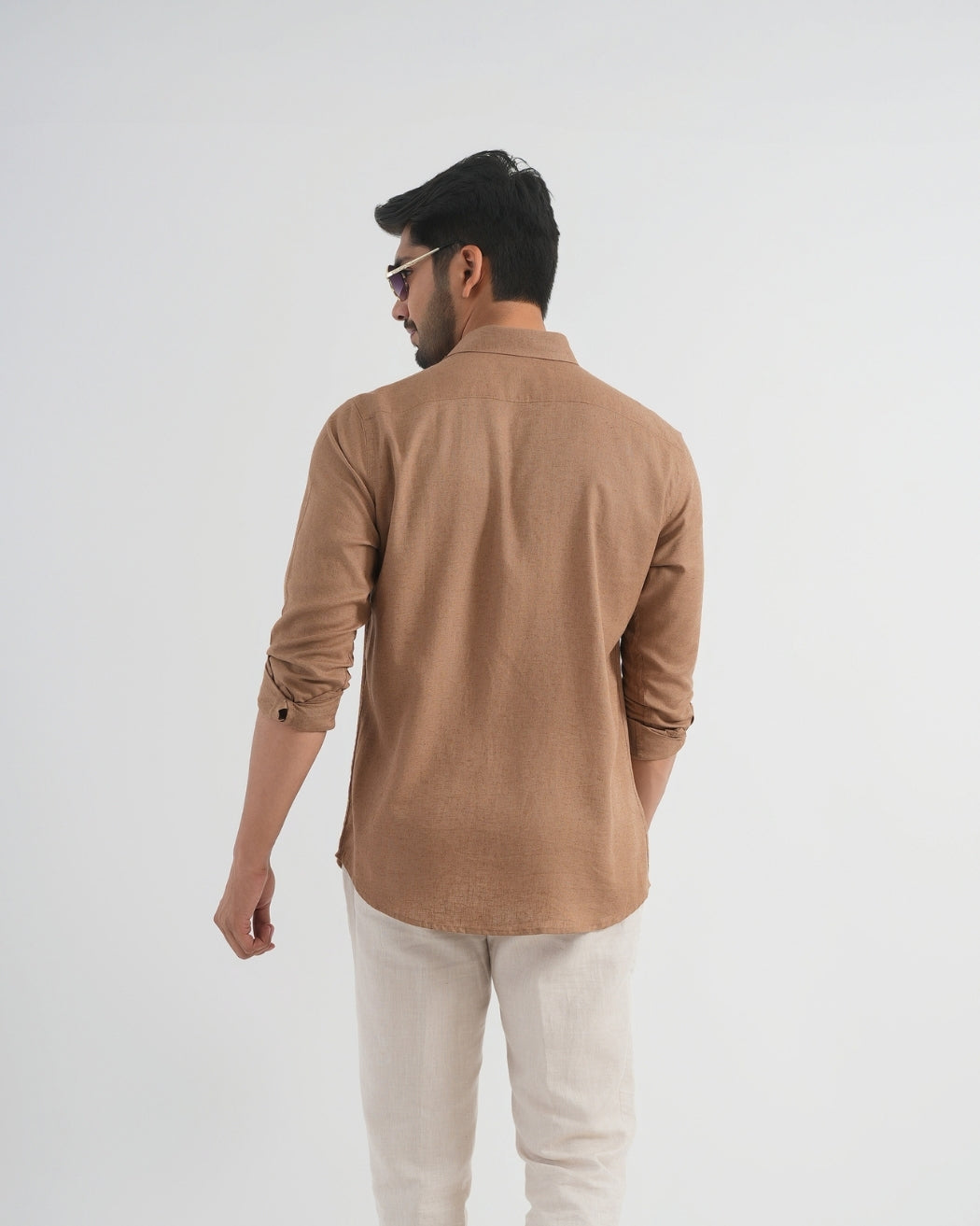 Man wearing a brown shirt and beige pants on a white background