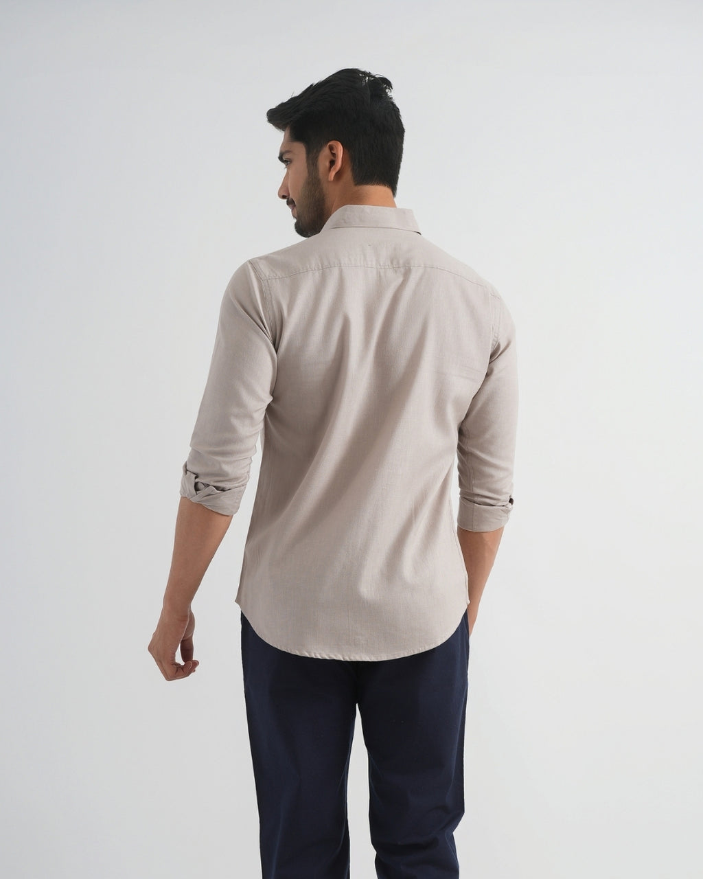 Man wearing a beige shirt and dark pants on a white background