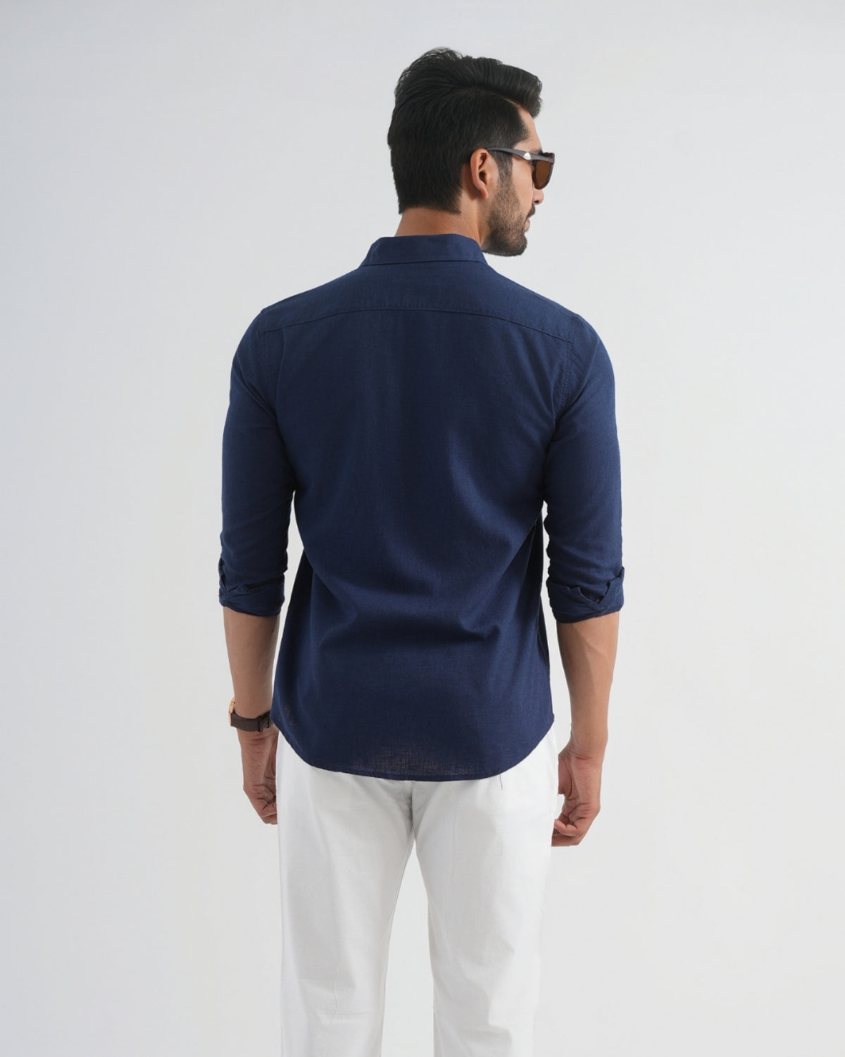 Man wearing a navy blue shirt and white pants on a light gray background