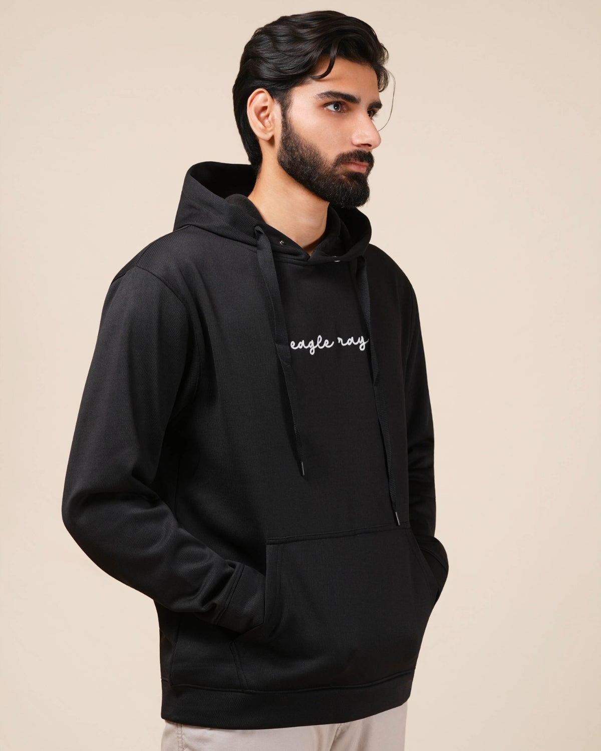 Man wearing a black hoodie with 'eagle ray' logo on a beige background
