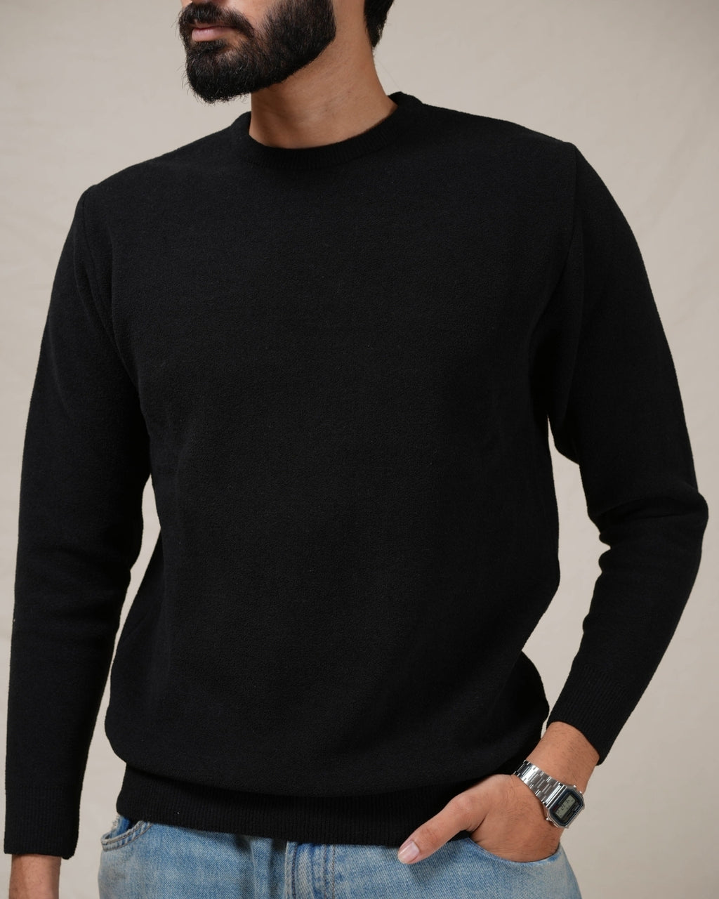 Person wearing a black sweater and blue jeans against a neutral background