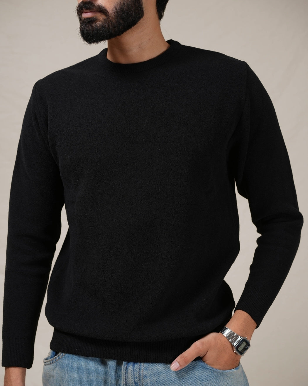 Person wearing a black sweater and blue jeans against a neutral background