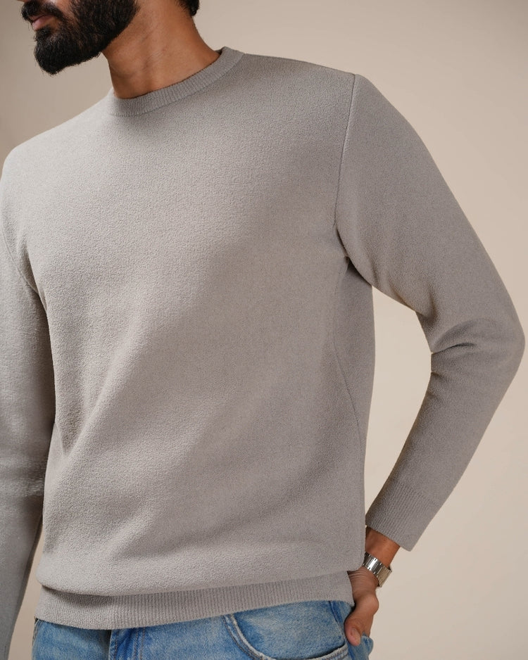 Man wearing a gray sweater and blue jeans against a beige background
