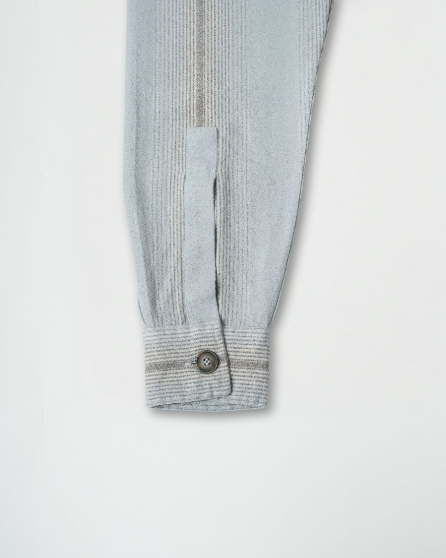 Close-up of a ribbed sweater sleeve with a button on a light gray background