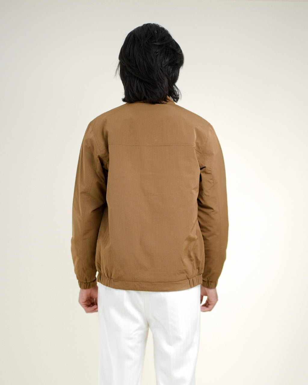 Person wearing a brown jacket and white pants against a plain background