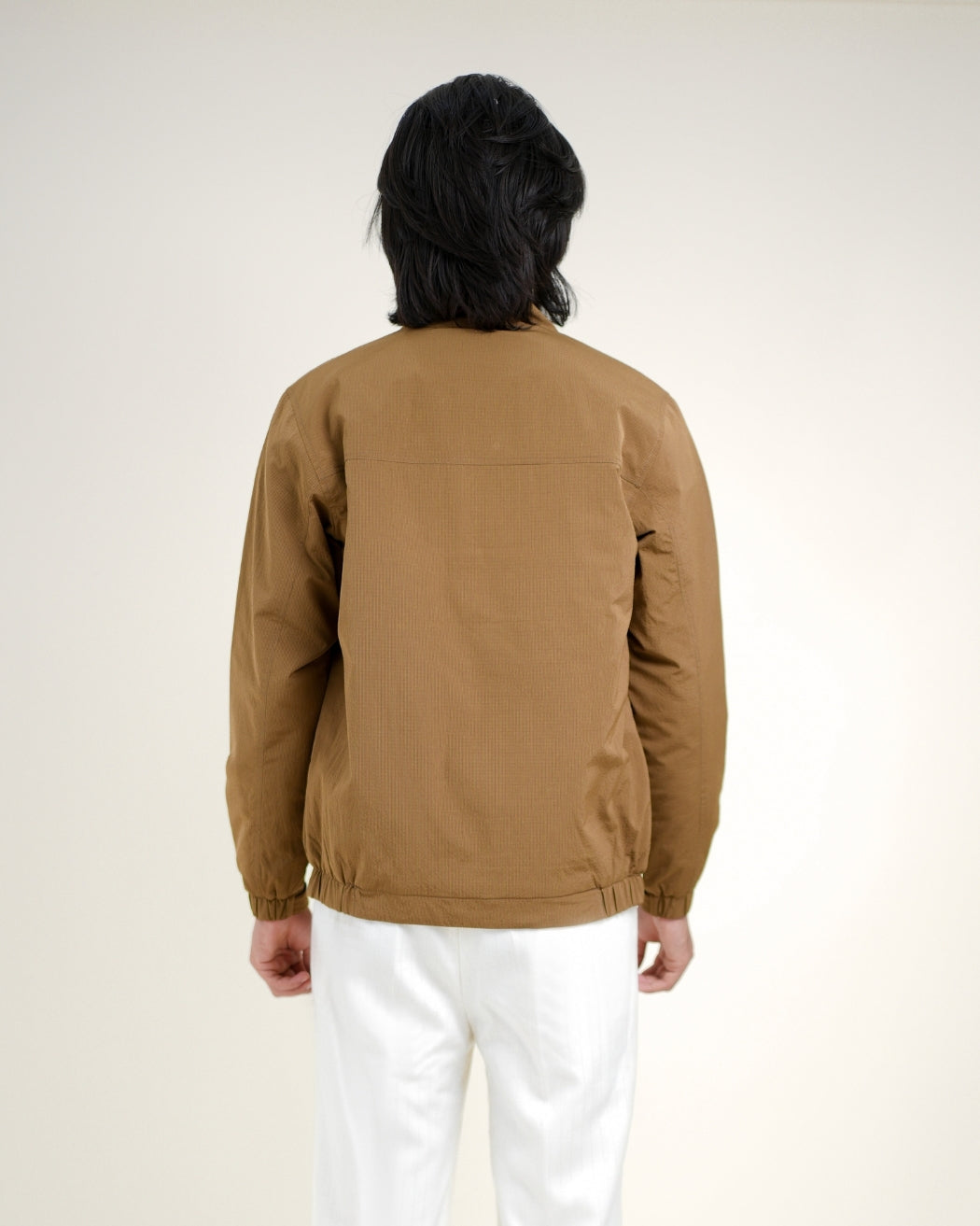 Person wearing a brown jacket and white pants against a plain background