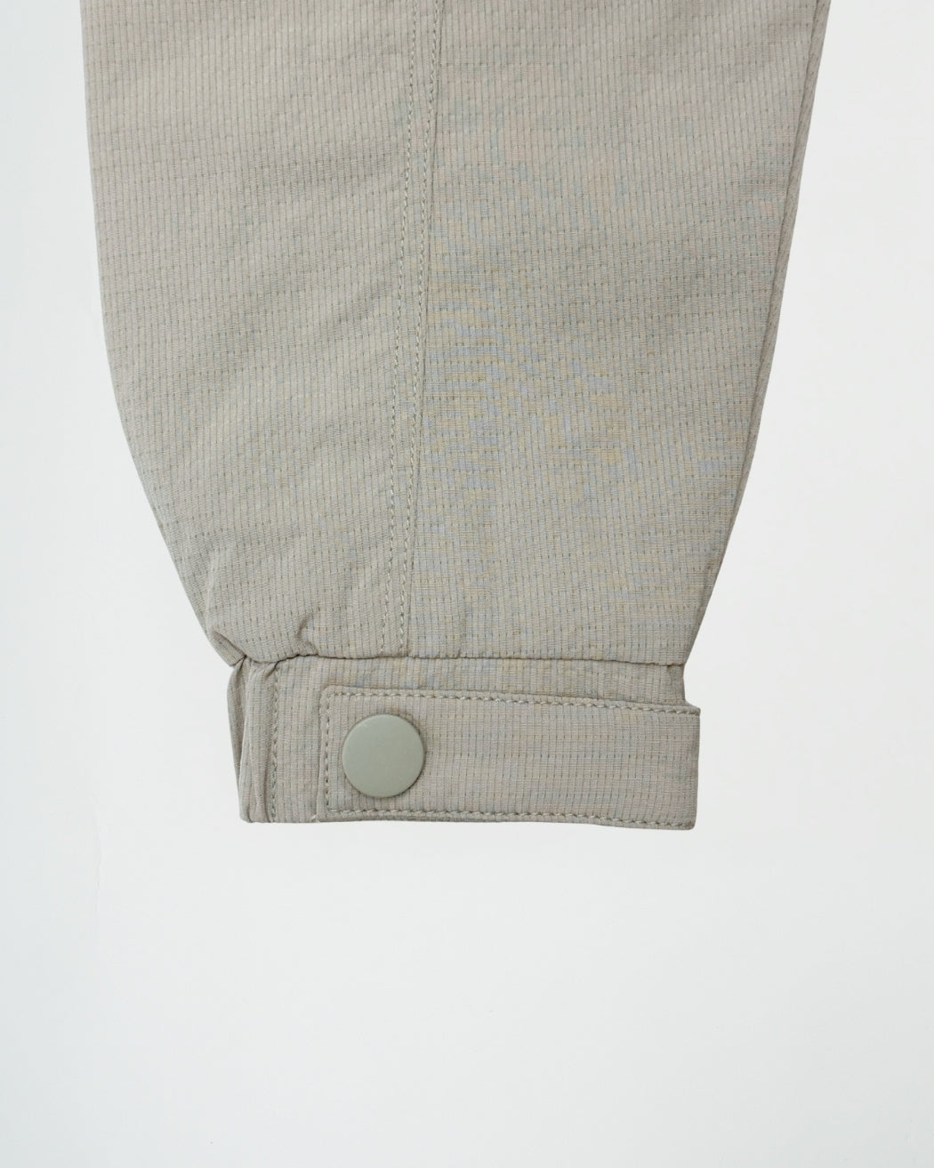 Close-up of a light gray corduroy pants cuff with a button on a white background