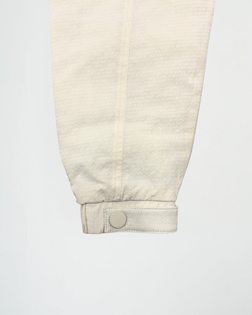 Close-up of a beige corduroy pants leg with a button on a white background
