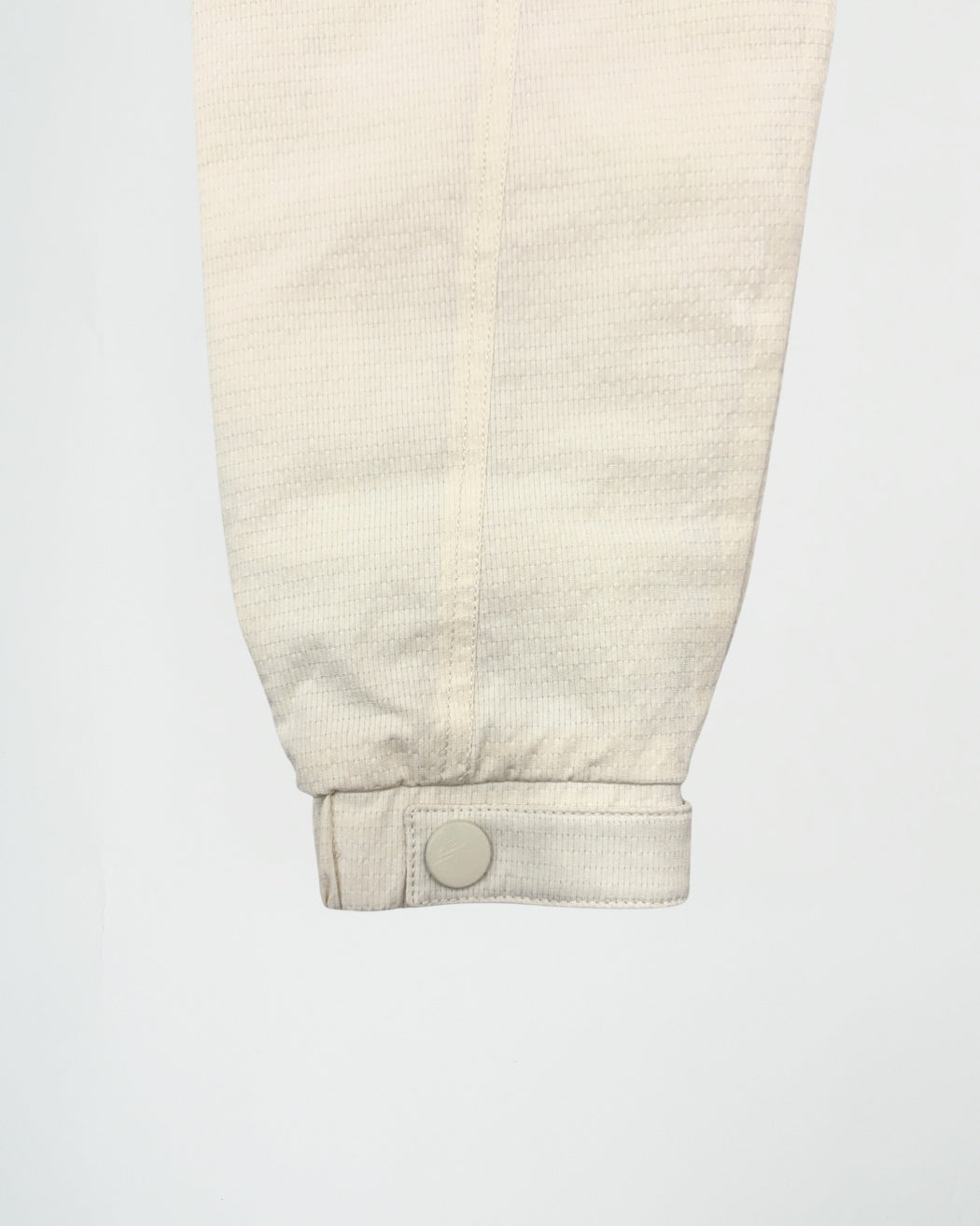 Close-up of a beige corduroy pants leg with a button on a white background