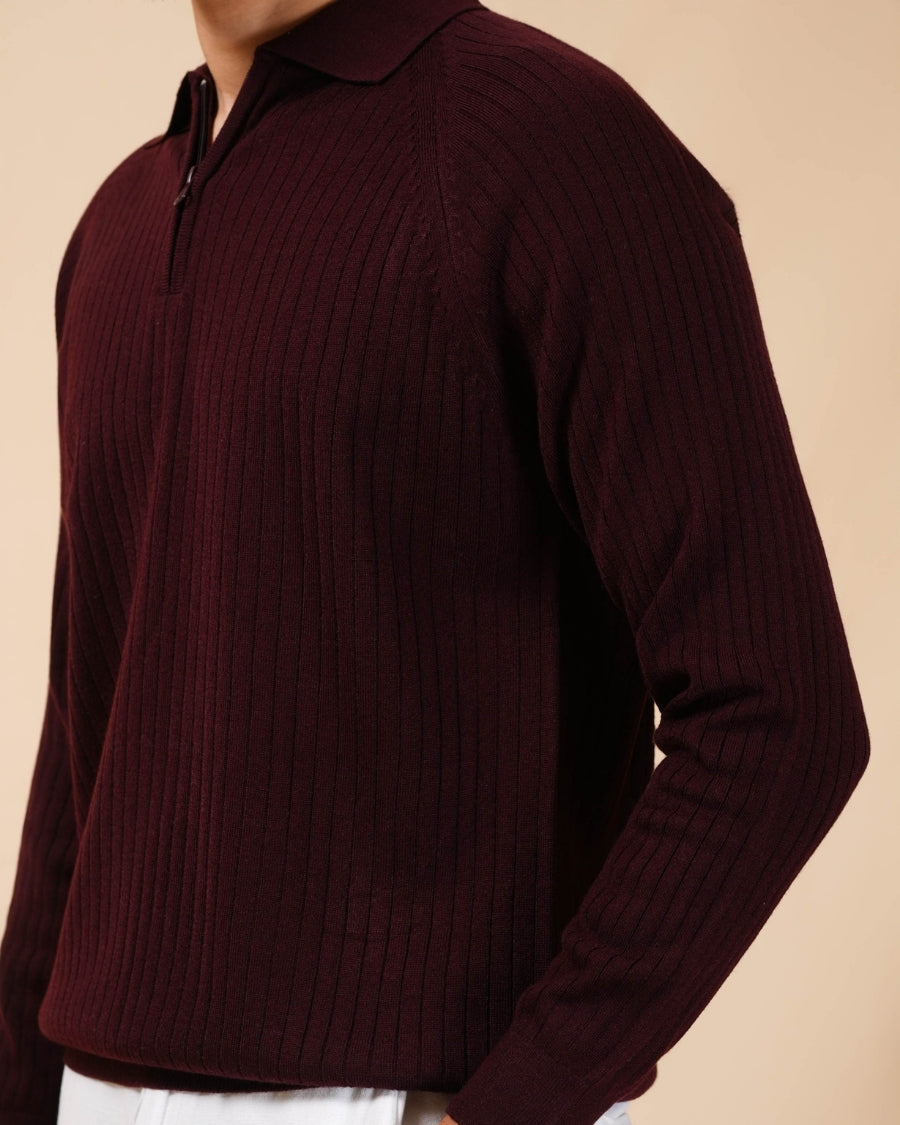 Man wearing a burgundy sweater and white pants against a beige background