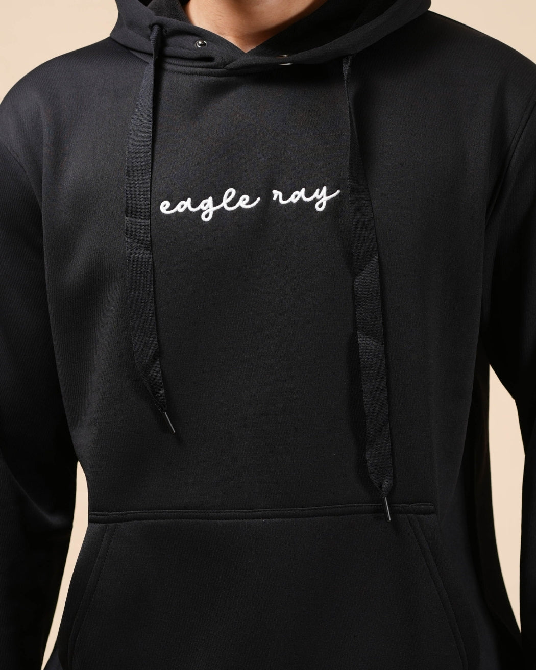 Man wearing a black hoodie with a logo on a beige background