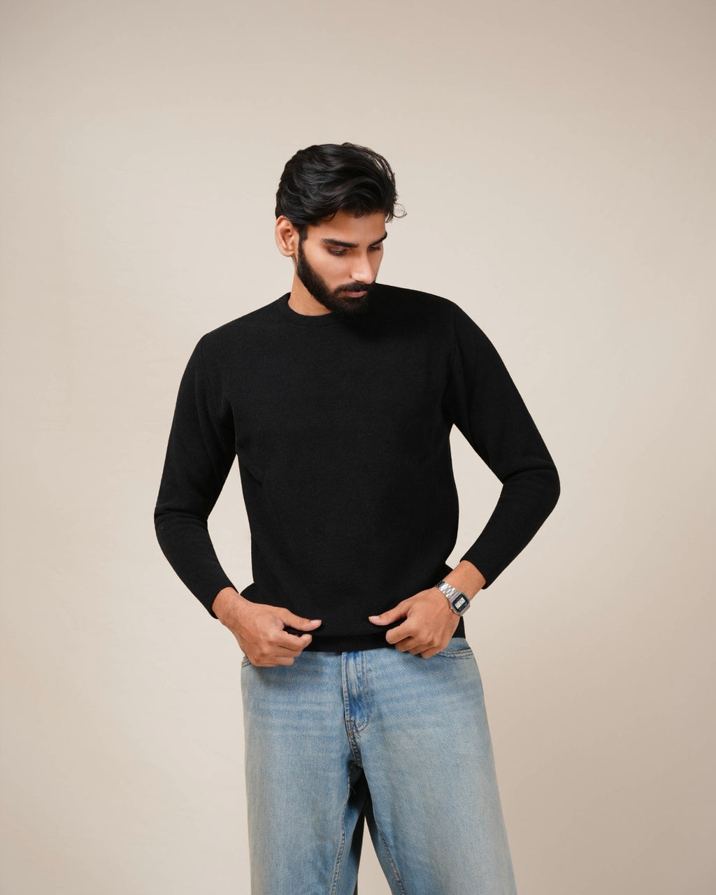 Man wearing a black sweater and light blue jeans against a beige background