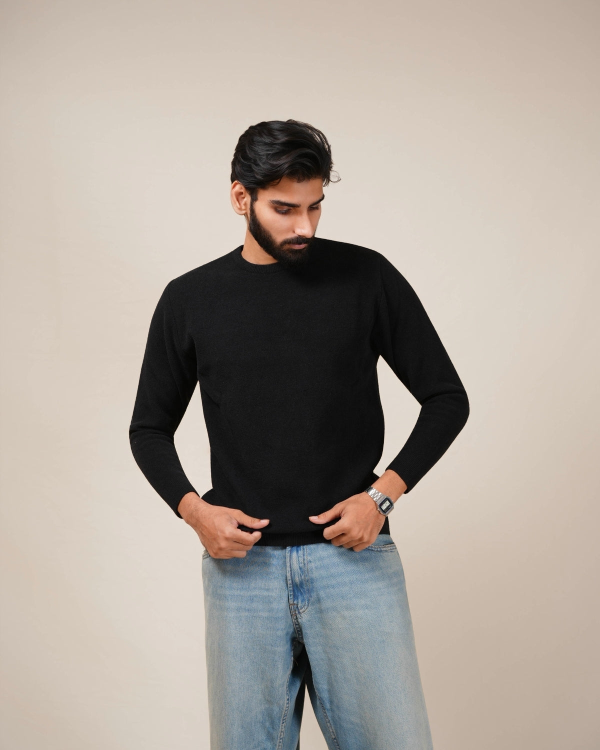 Man wearing a black sweater and light blue jeans against a beige background