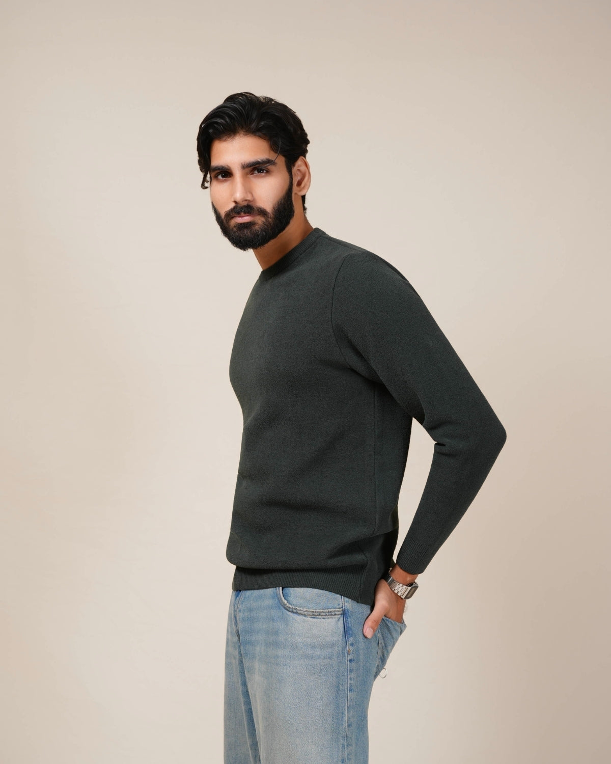 Man wearing a dark gray sweater and light blue jeans against a beige background