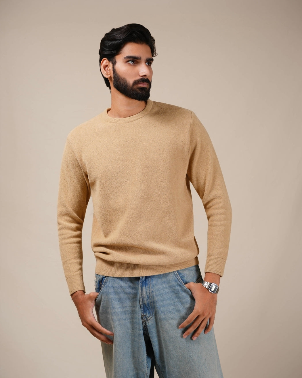 Man wearing a beige sweater and blue jeans against a beige background