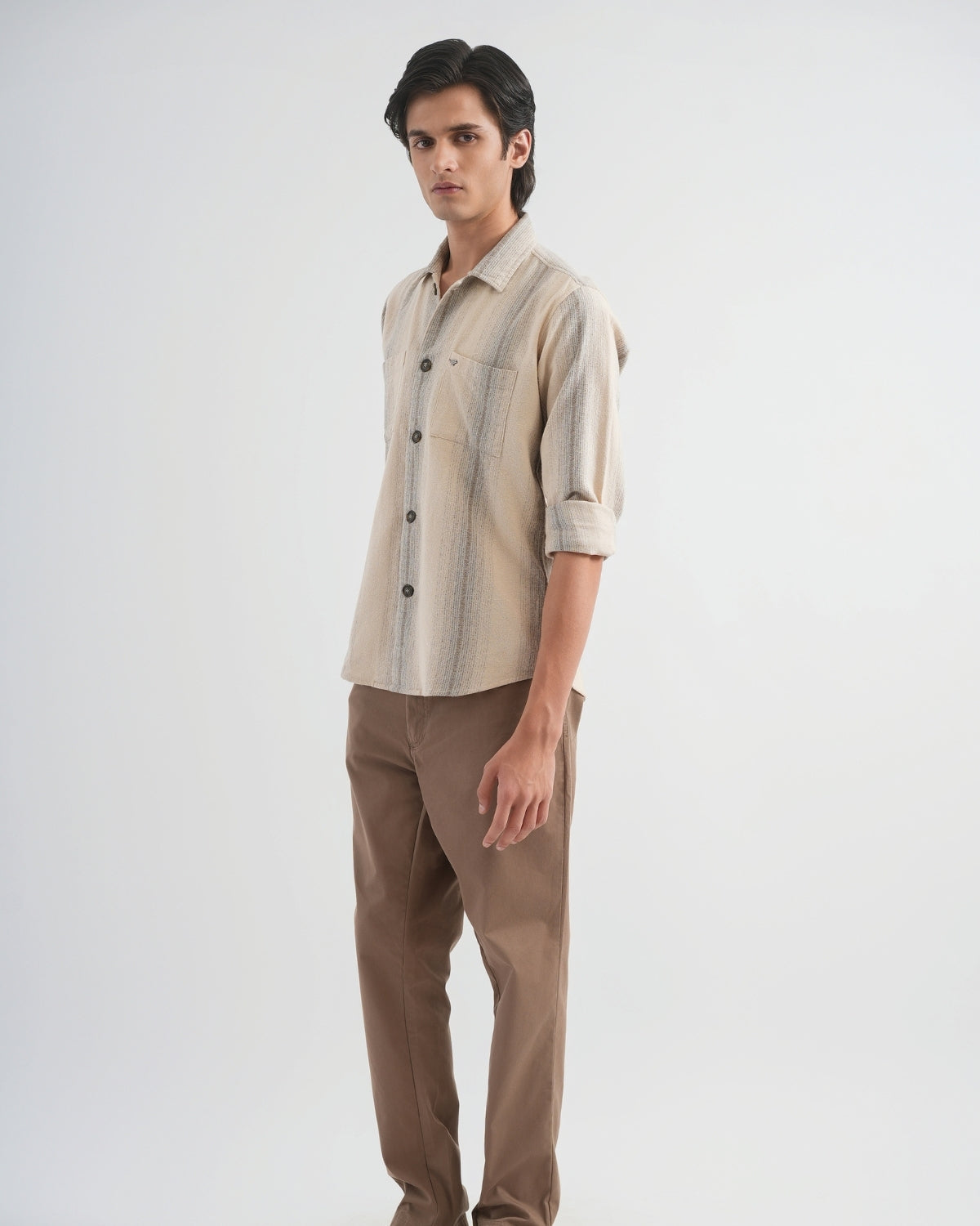 Man wearing a beige and brown striped shirt with brown pants on a white background
