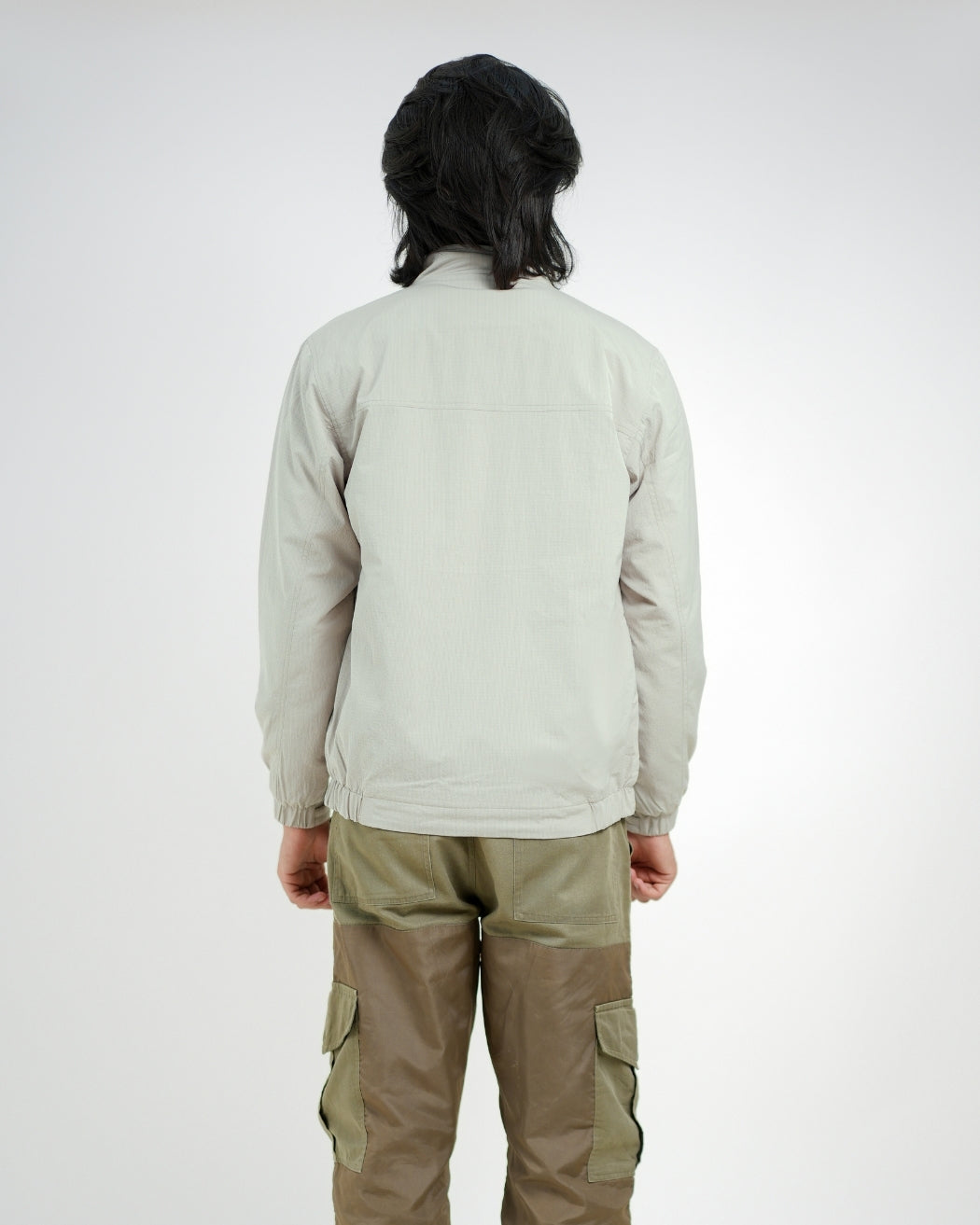Person wearing a light gray jacket and beige pants on a white background