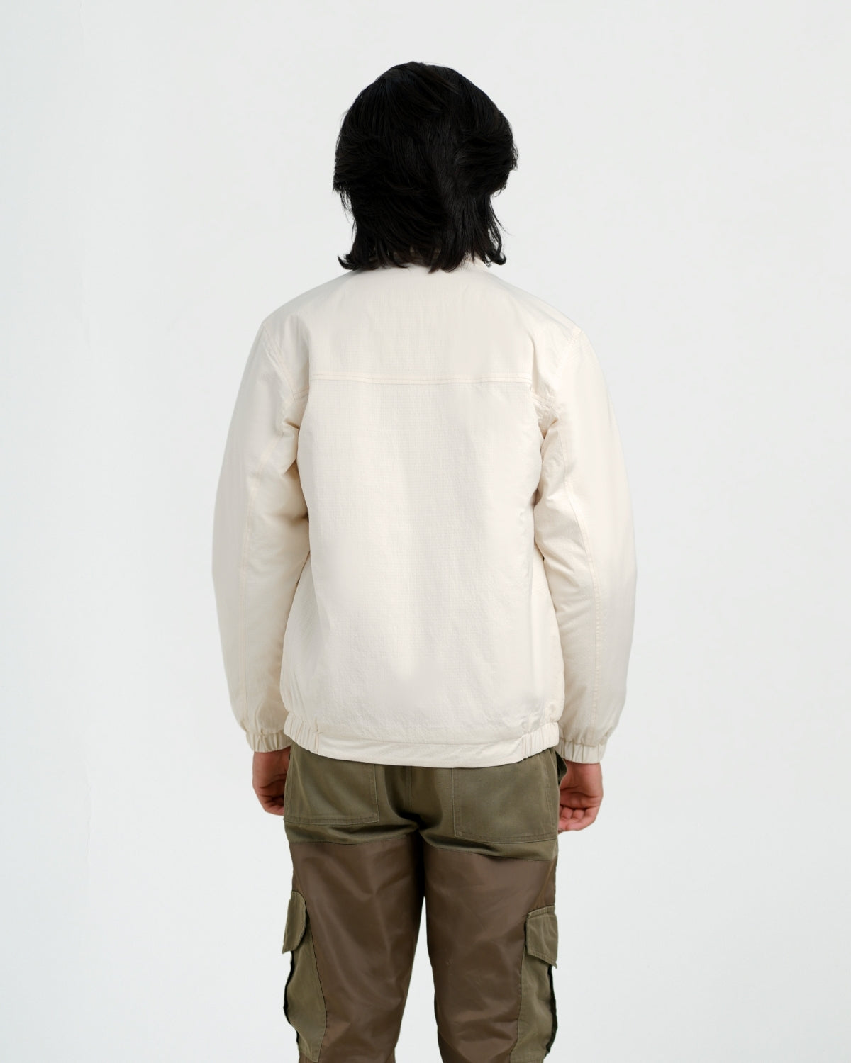 Person wearing a cream jacket and green cargo pants on a white background