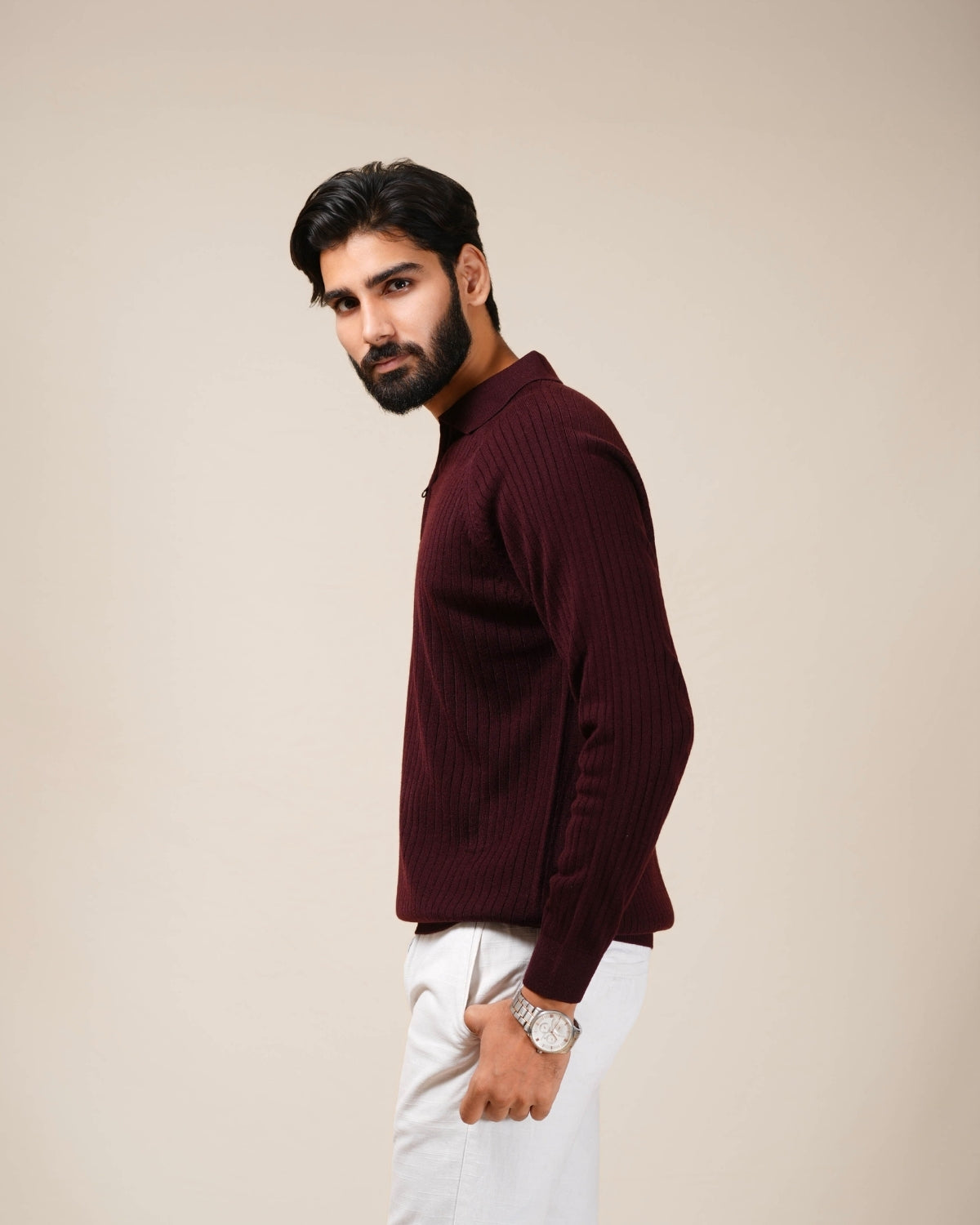 Man wearing a maroon sweater and white pants against a beige background