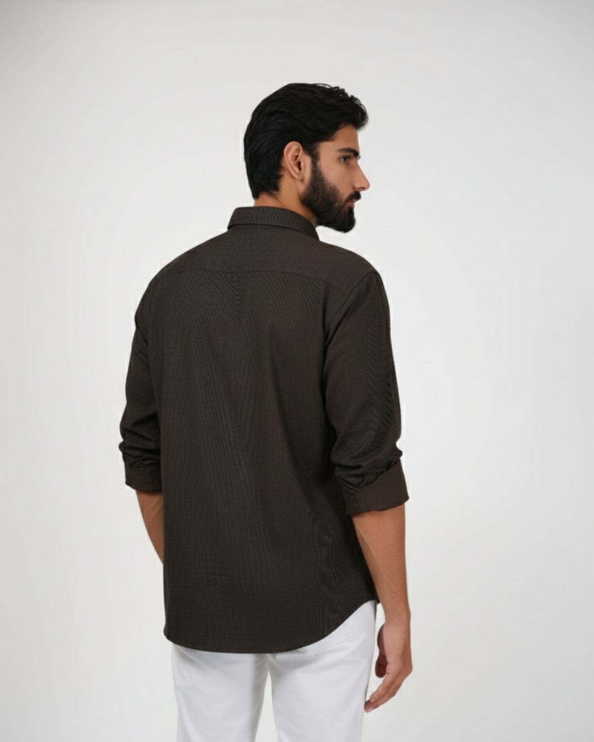 Man wearing a dark brown shirt and white pants on a light gray background