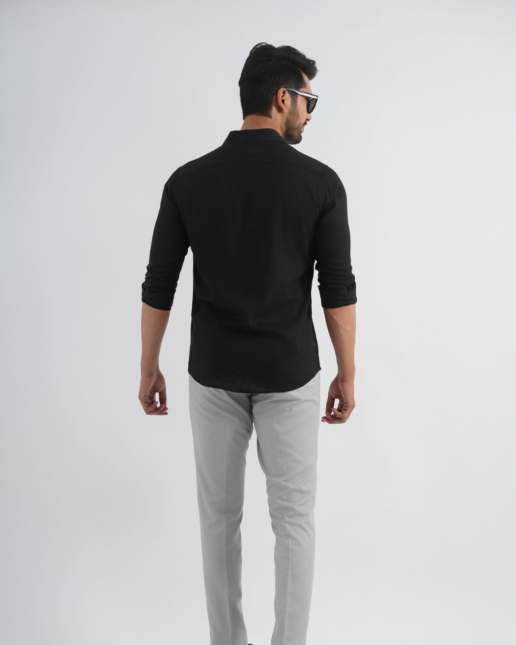 Man wearing a black long-sleeve shirt and light gray pants on a white background