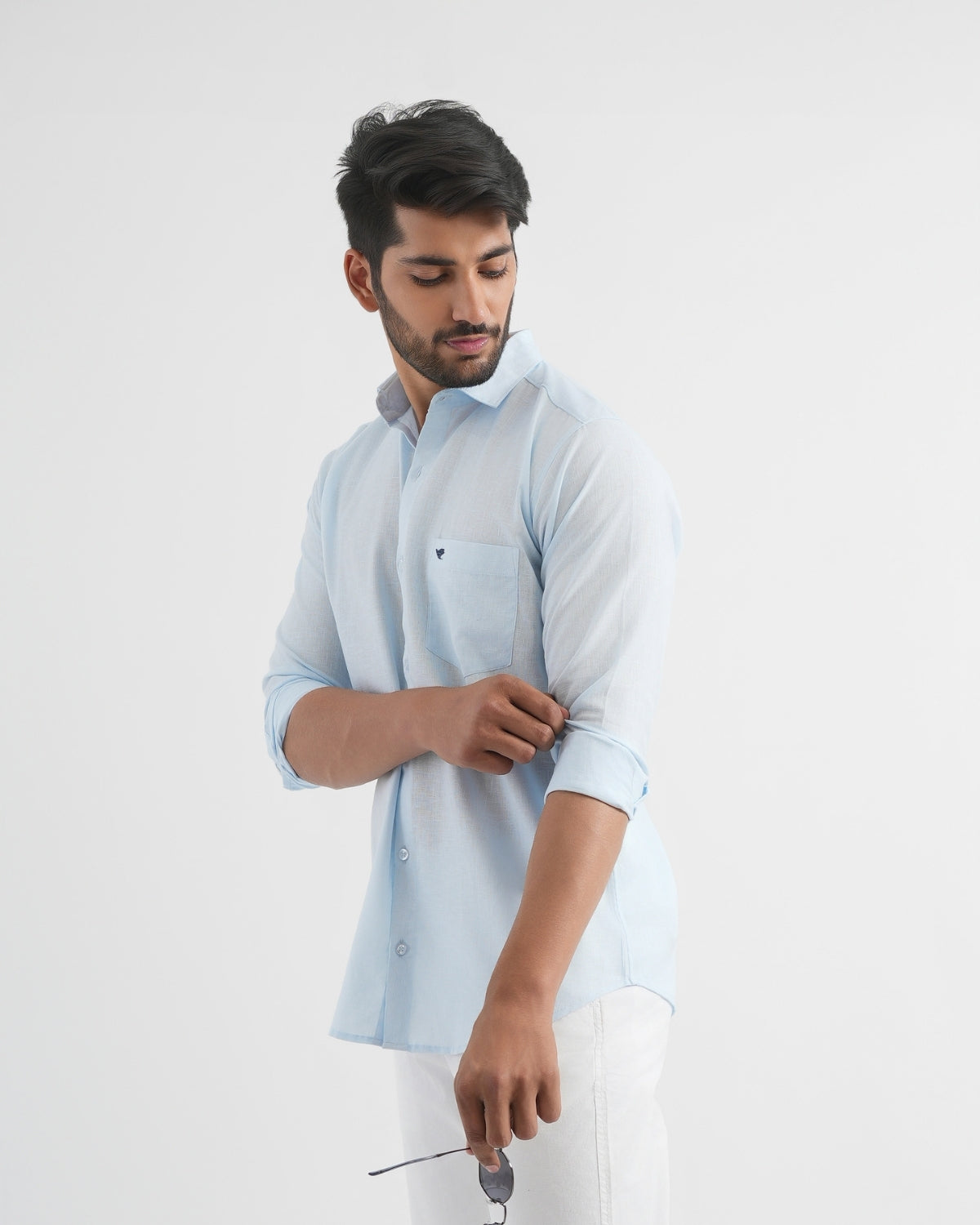 Man wearing a light blue shirt with rolled-up sleeves against a white background